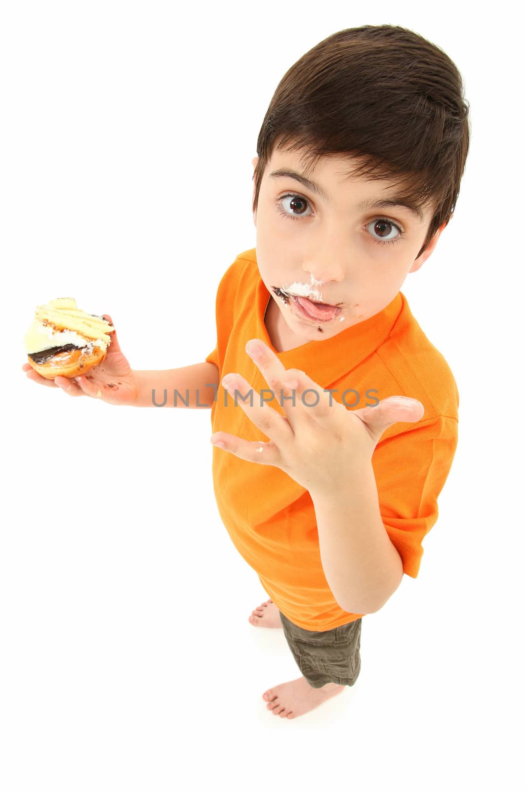 Attractive 8 year old boy standing with donut and cake licking food off fingers.