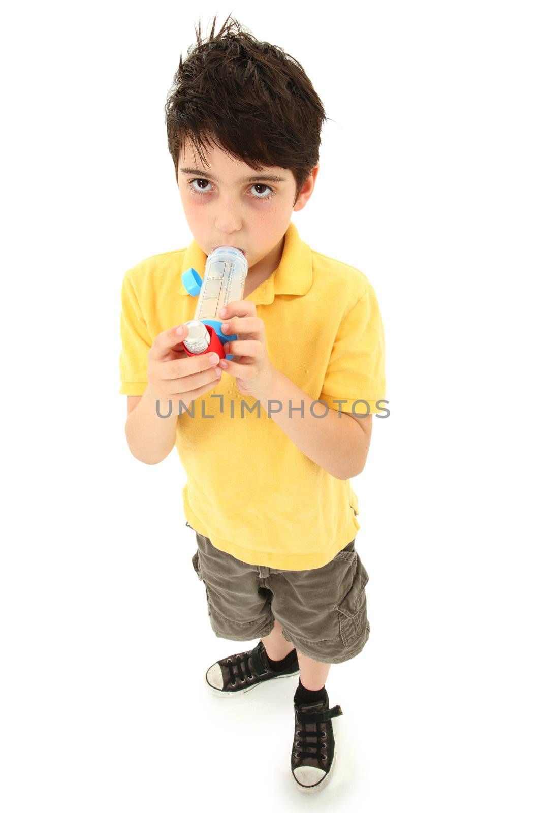 Sick young boy child using asthma inhaler with spacer chamber over white.  Has periorbital hyperpigmentation.