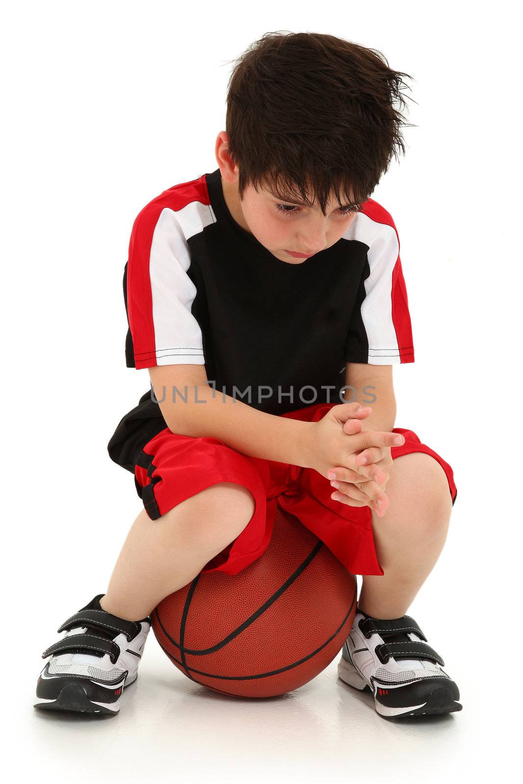 Sad elementary school boy sitting on basketball sad crying expression on face.