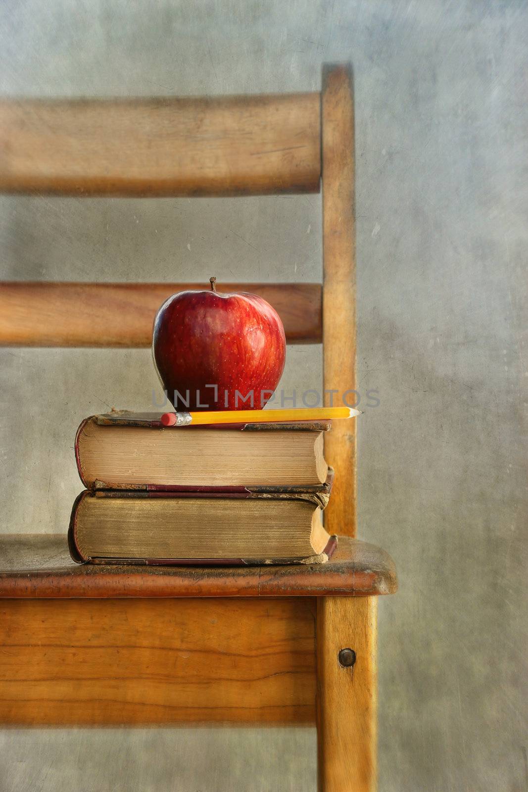 Apple and old books on school chair by Sandralise