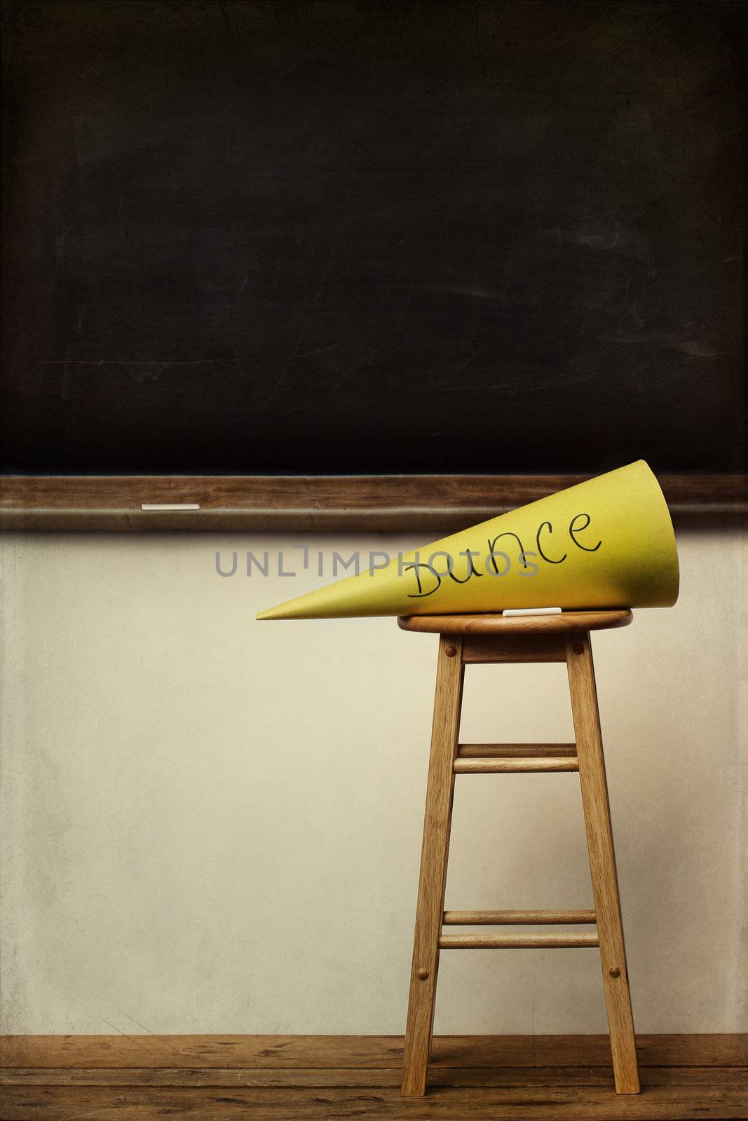 Yellow dunce hat on stool with chalkboard in background