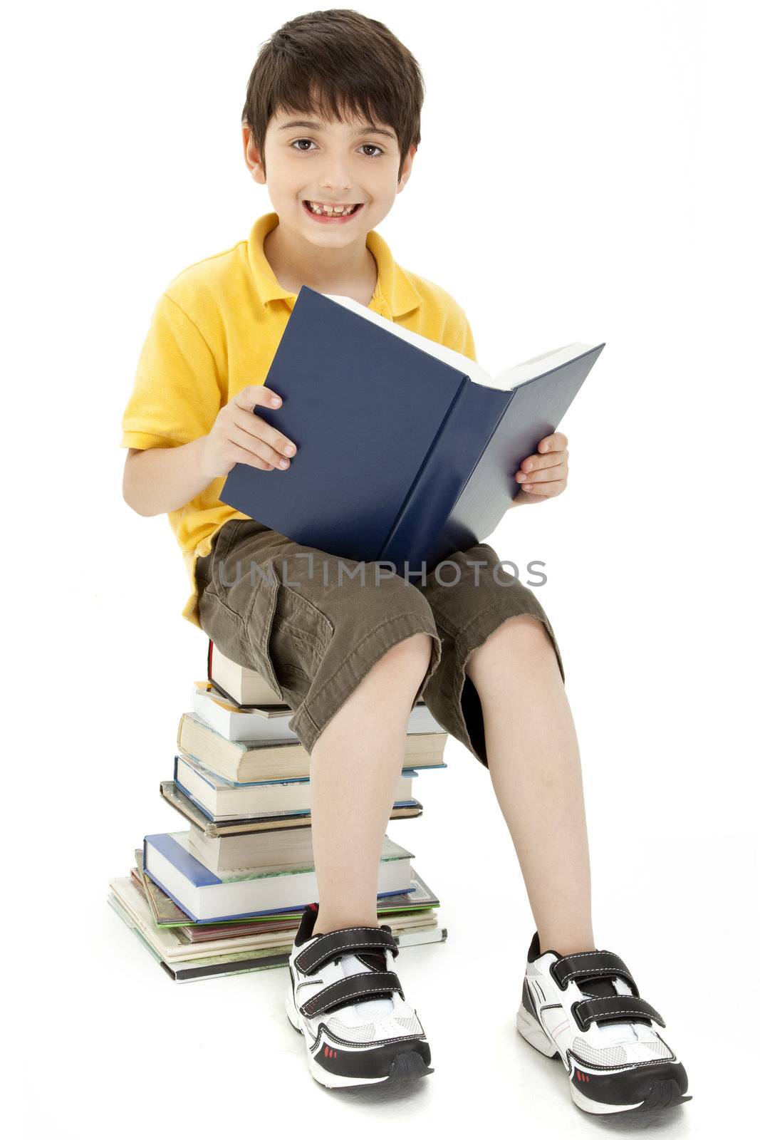 Attractive boy child sitting on large stack of books reading.