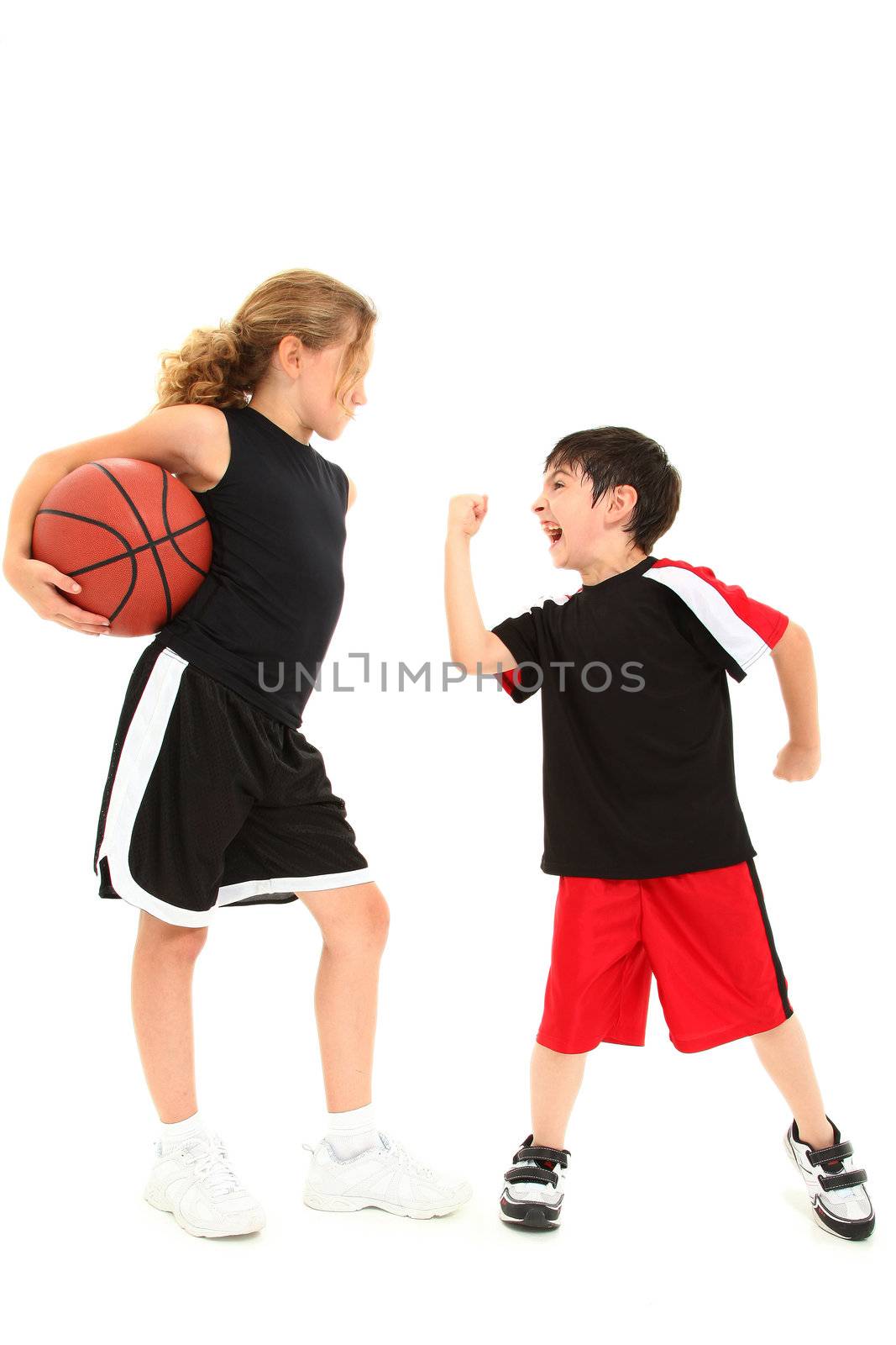 Adorable short boy child shaking fist at taller girl basketball player over white.