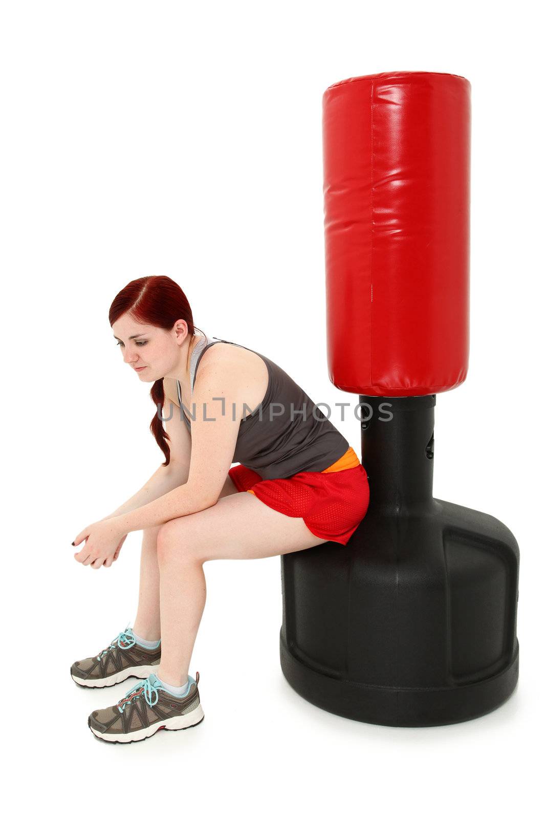 Attractive 19 year old woman sitting resting on free standing heavy bag after workout.