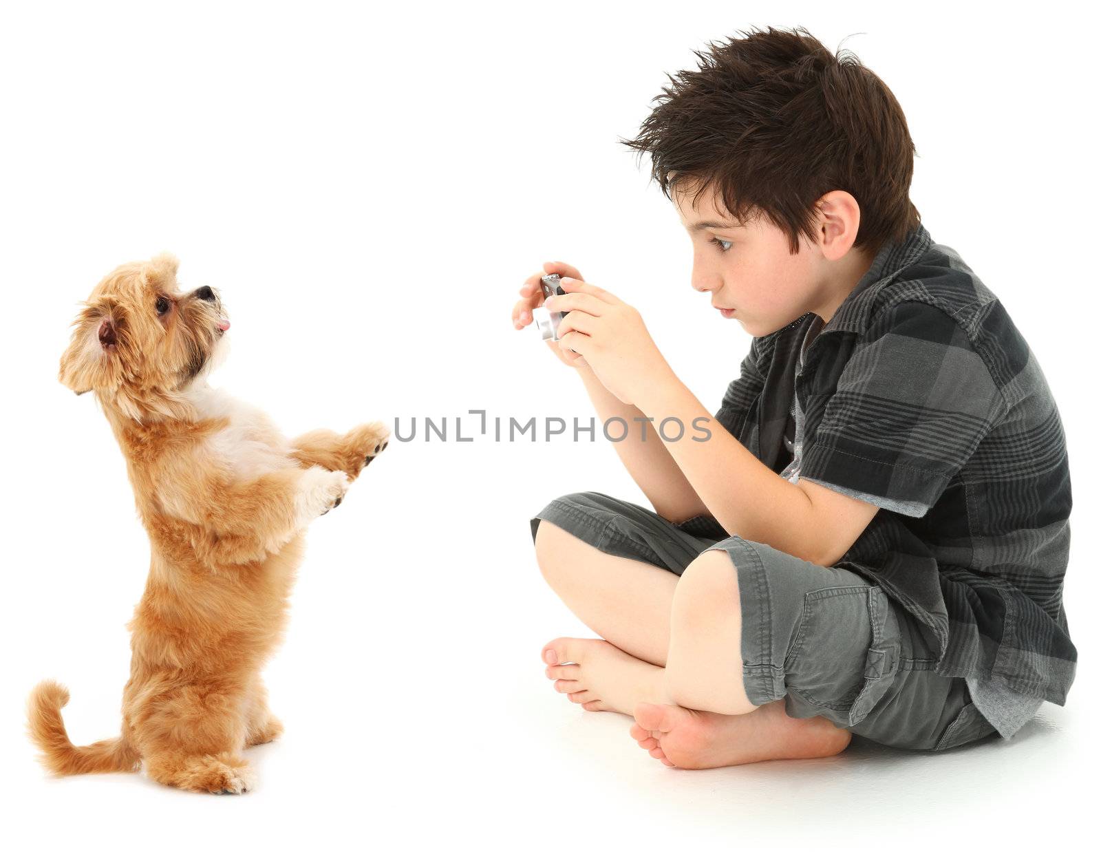 Adorable 8 year old boy shooting photos of his dog with digital camera over white background.