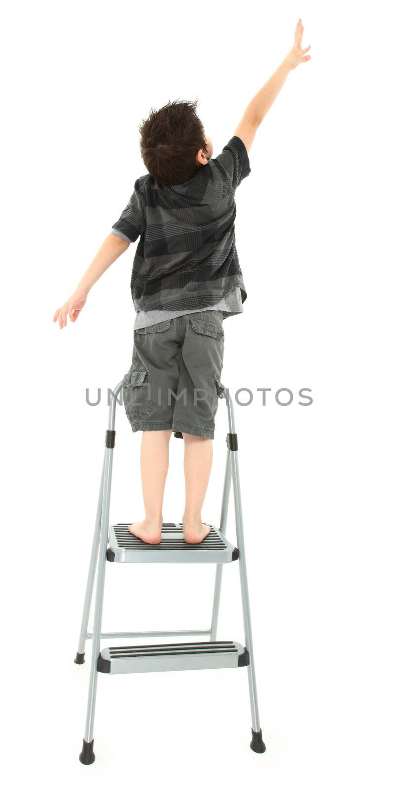 Young boy on step ladder reaching up over white background.