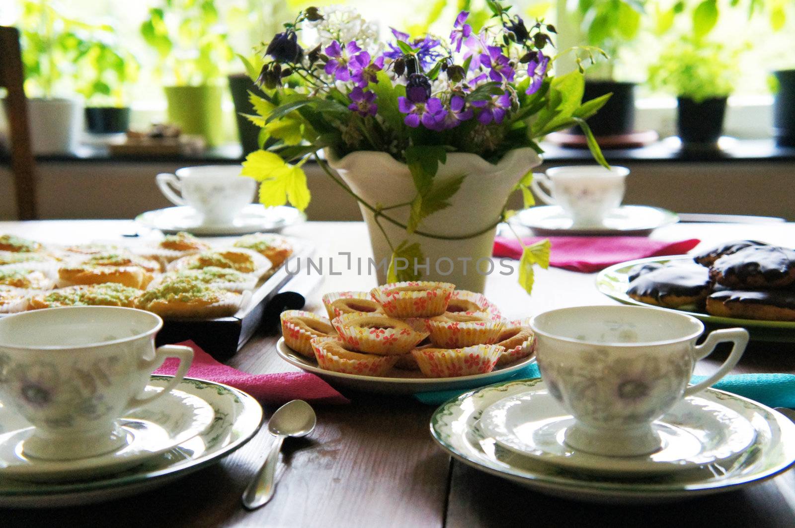 A table set with beautiful old copper coffee and buns and a vase with flowers are at the Center, in the background is parts of a window