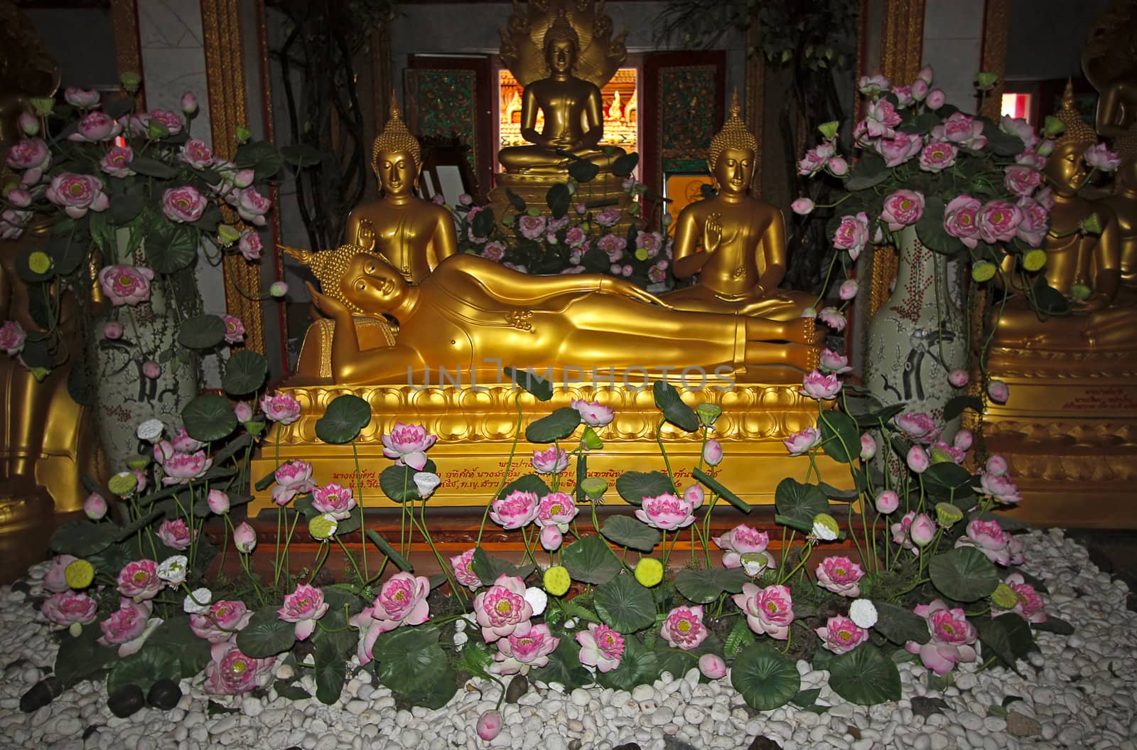 Gold statues of Buddha in  Buddhist temple on  background of flowers, Thailand.