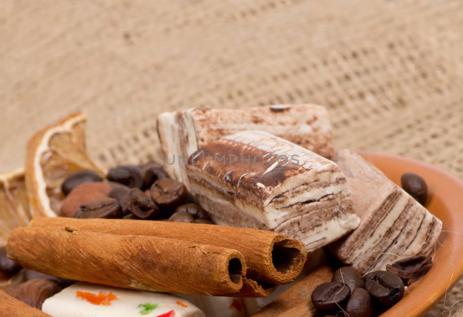 Sweets, cinnamon, nuts and coffee beans on a saucer, on burlap background.