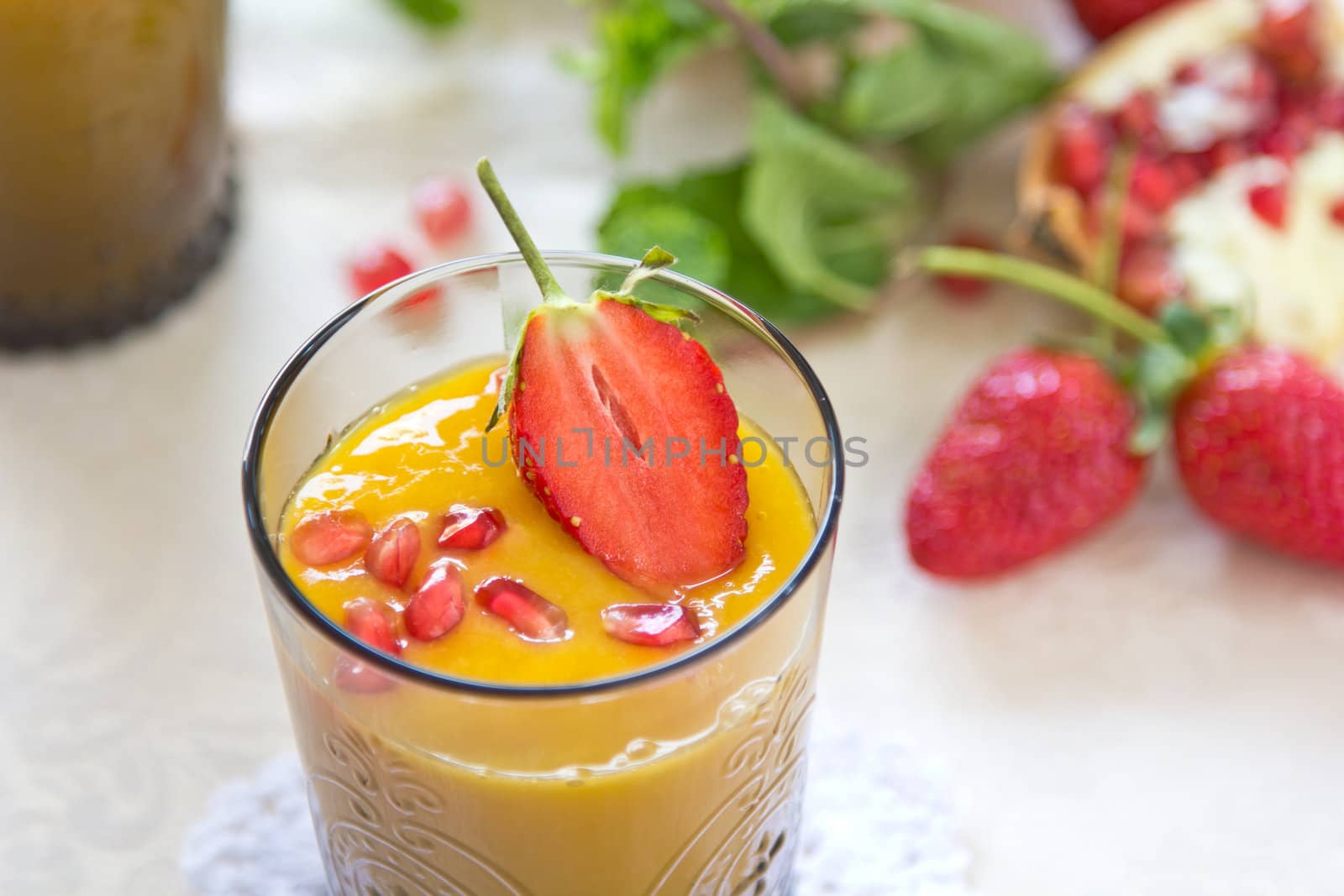 Mango and pineapple smoothie with fresh pomegranate and strawberry on top