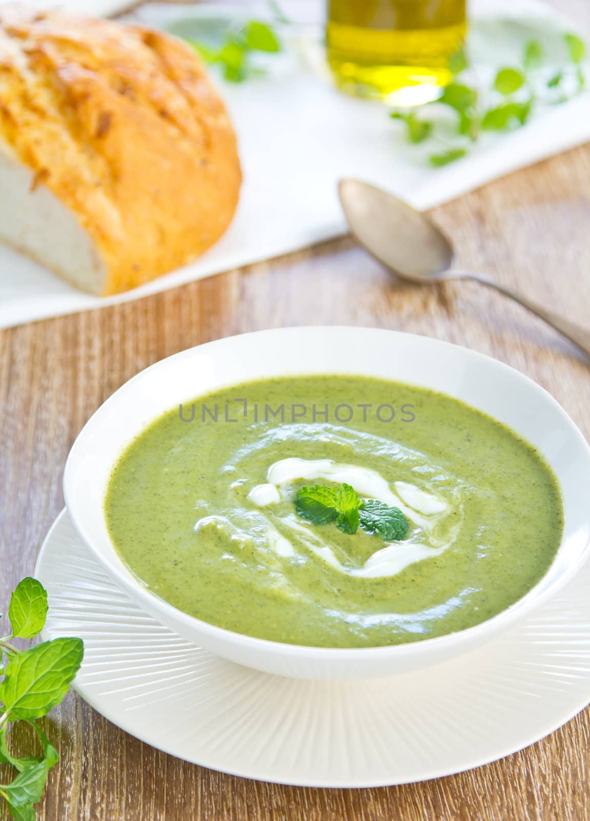 Pea,mint and celery soup with cream on top by a loaf of bread