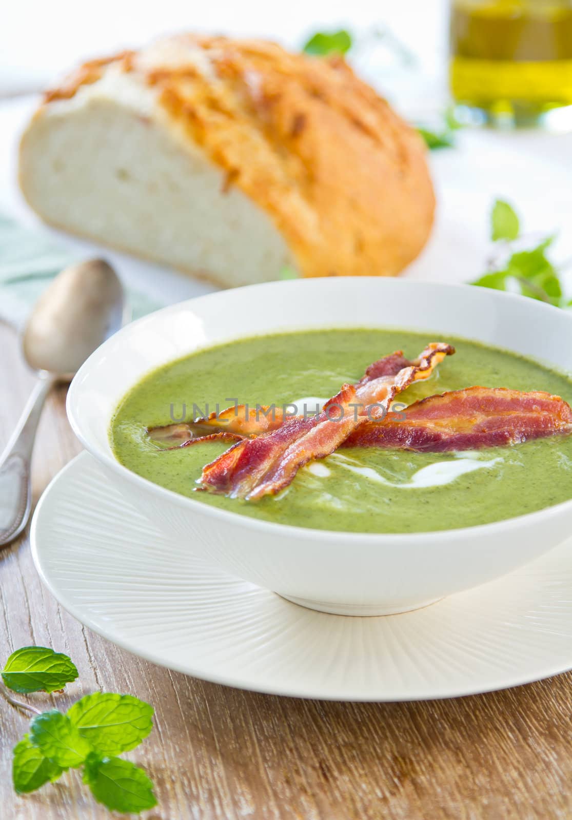 Pea,mint and celery soup with cream and bacon on top by a loaf of bread