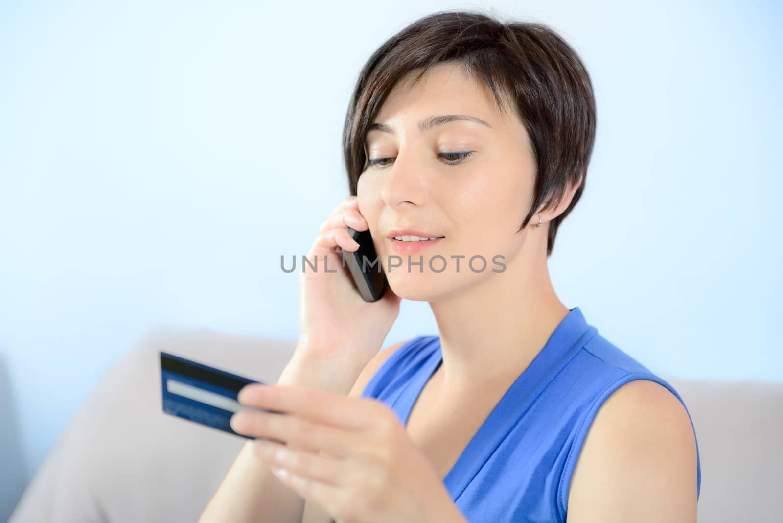 Young woman calling on mobile phone and holding a credit card.