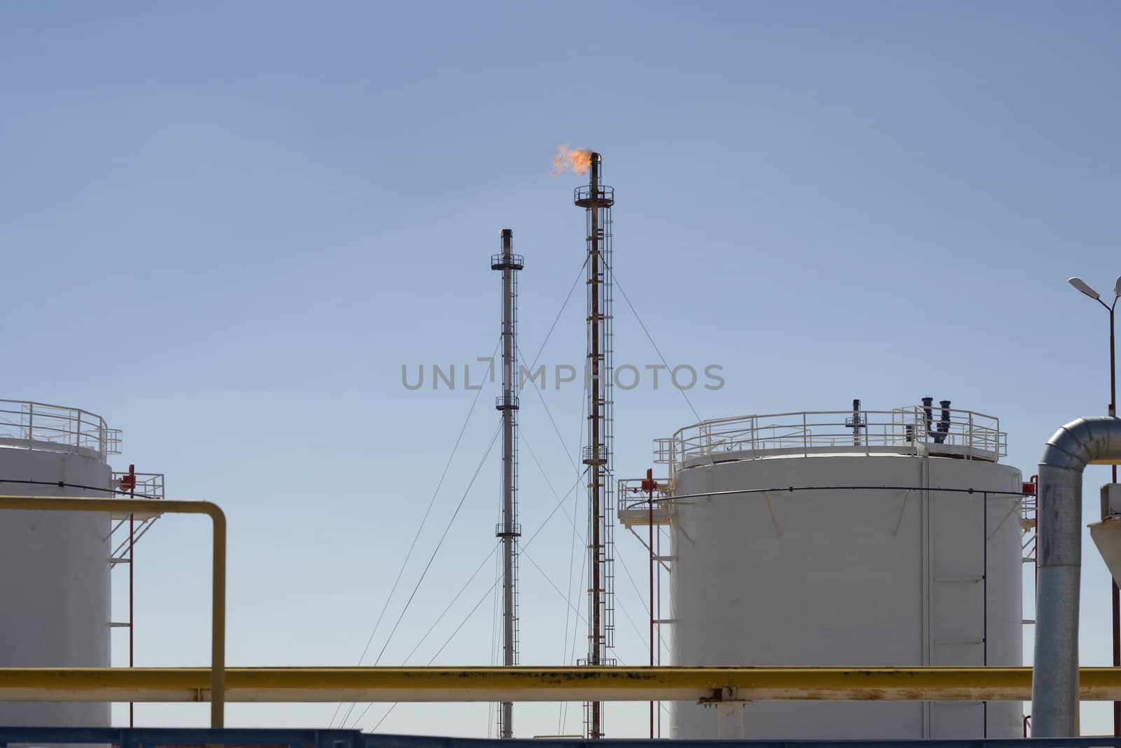 Storage tanks and gas towers with burning flames at an industrial petrochemical plant extracting fossil fuel from the earth