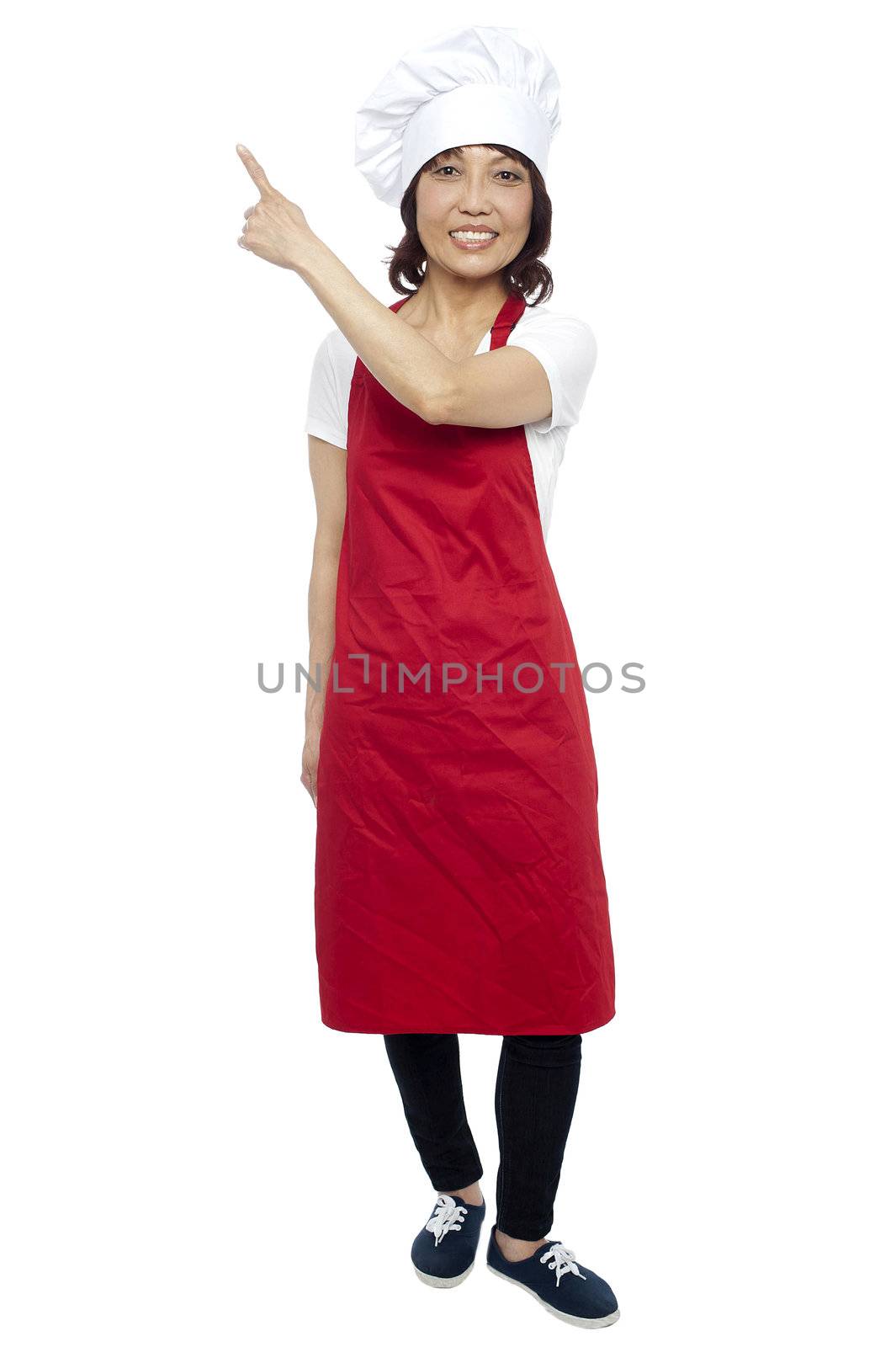 Beautiful female chef pointing at the copy space. Full length shot