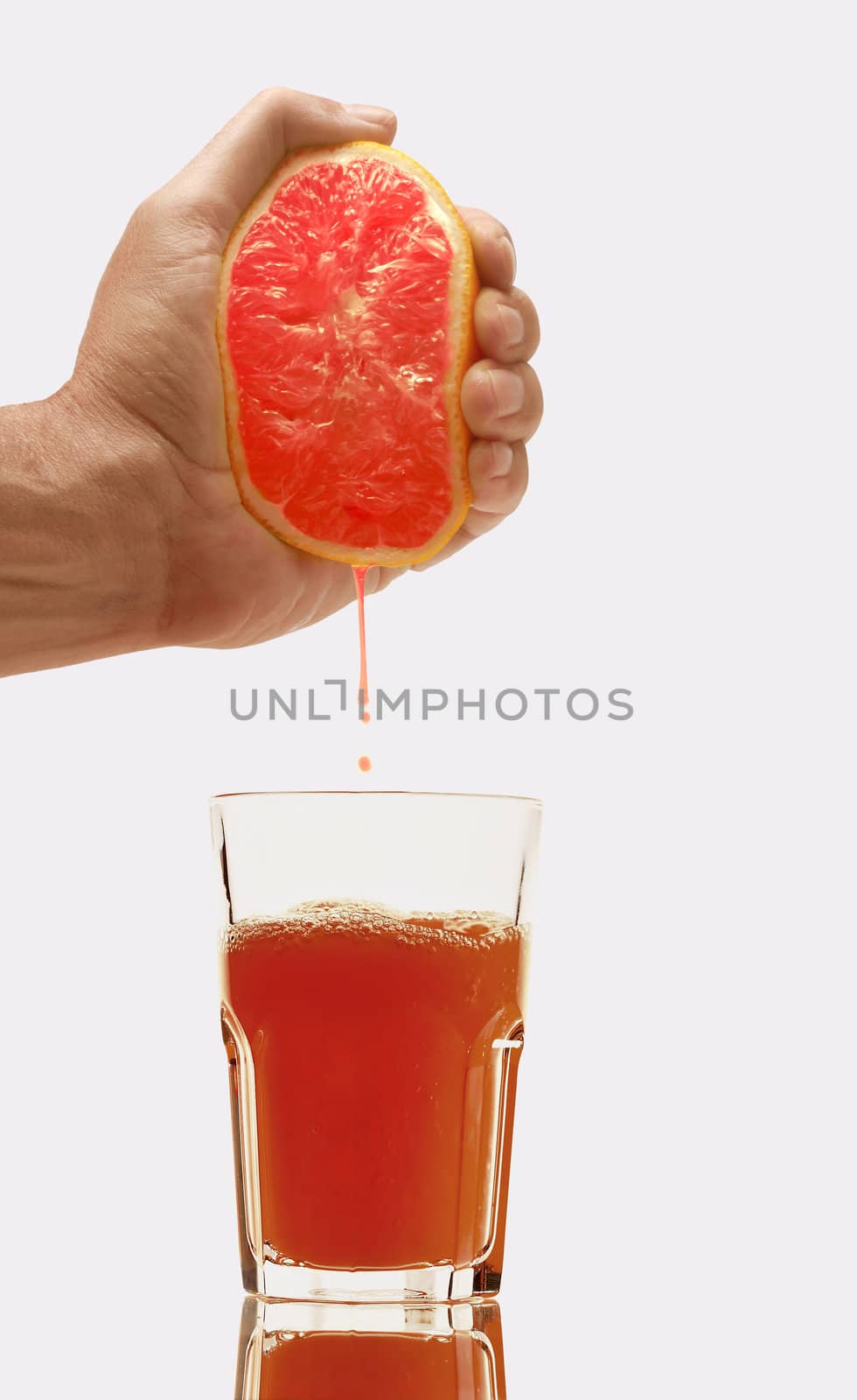 Glass of fresh grapefruit juice and hand with half of grapefruit on white background