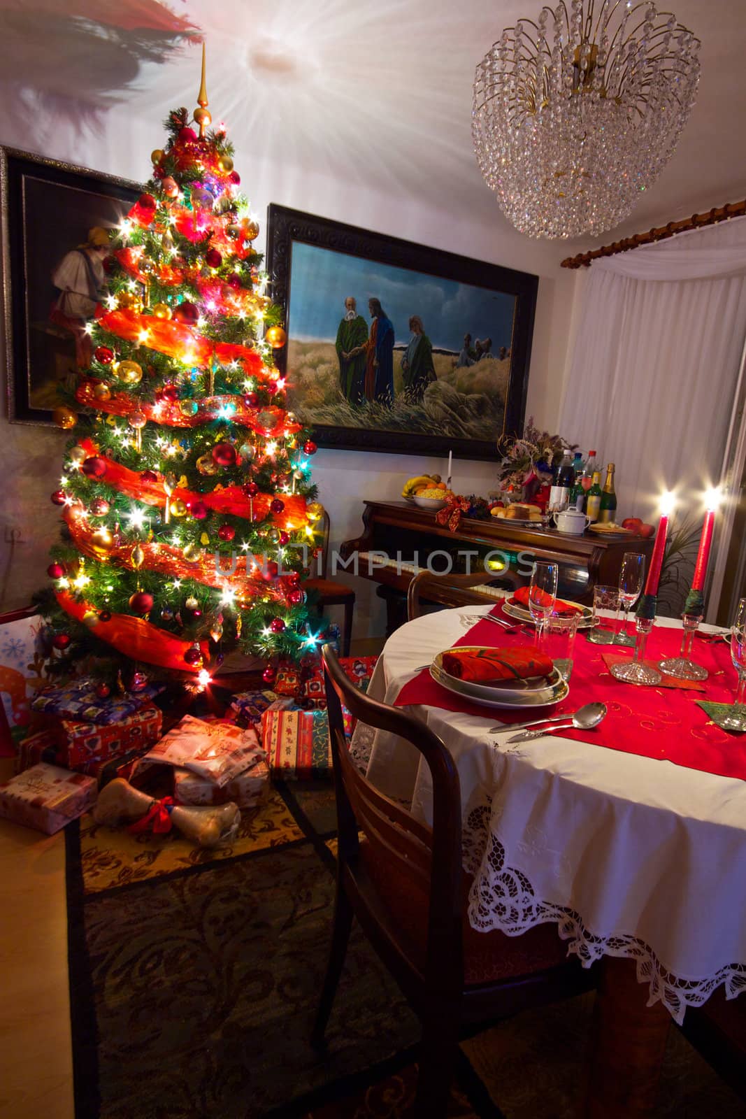 Cozy room with presents under decorated Christmas tree, old piano and table ready for Christmas dinner