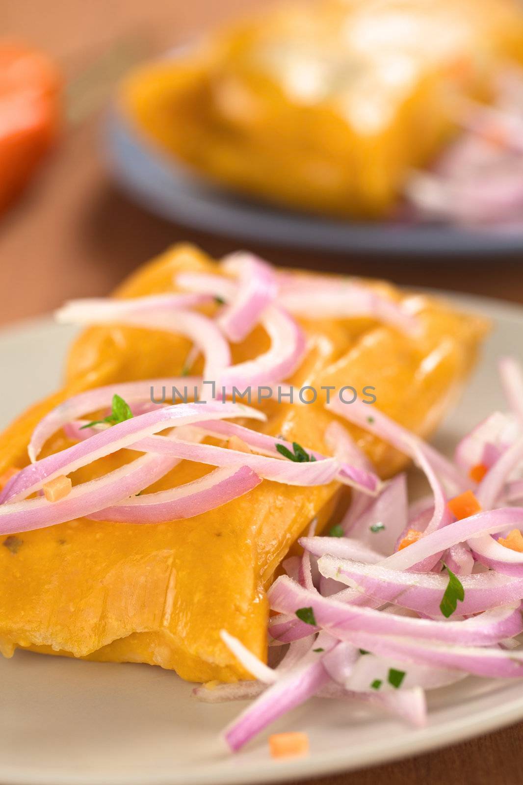 Peruvian tamales (traditionally eaten for breakfast on Sundays) made of corn and chicken and served with salsa criolla (onion salad) (Selective Focus, Focus on the front of the onion salad on top of the tamale)