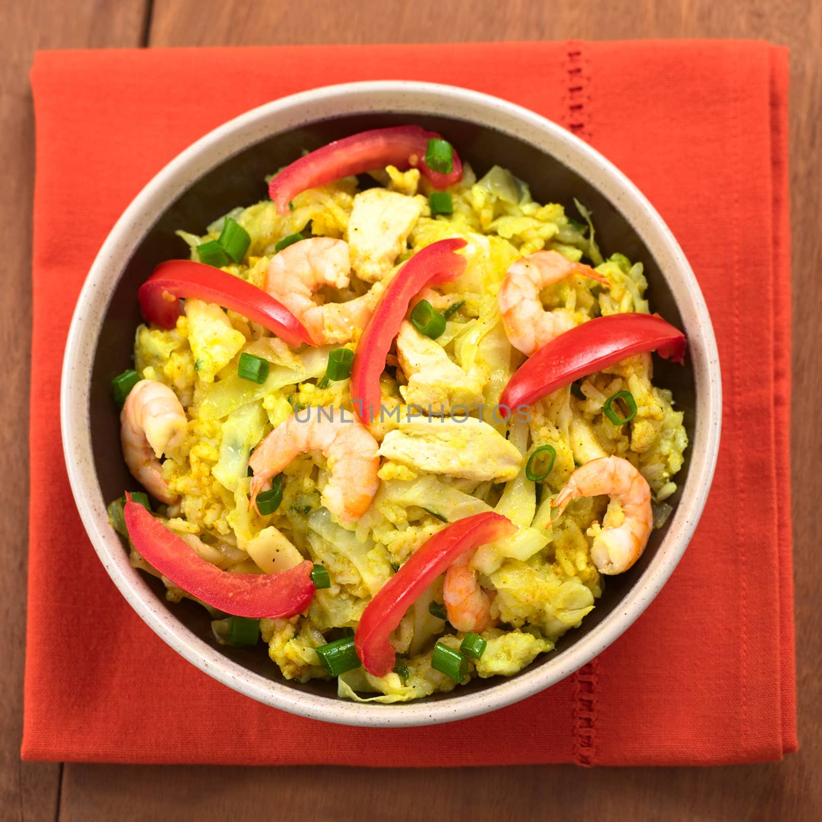 Bowl of spicy rice dish with cabbage, chicken and shrimp, garnished wih tomato slices and scallion (Selective Focus, Focus on the lower part of the dish)