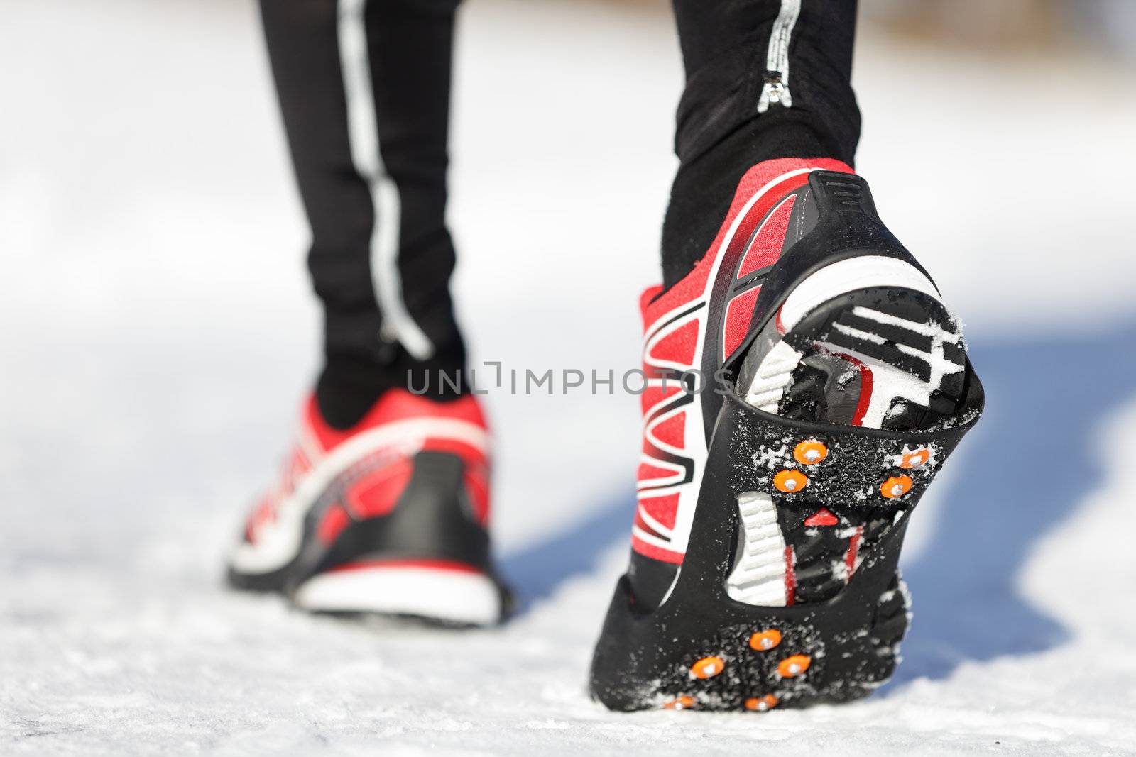 Running shoes in snow with grip soles or traction cleats with metal spikes for anti slip grip when walking or running. Man winter running in snow.