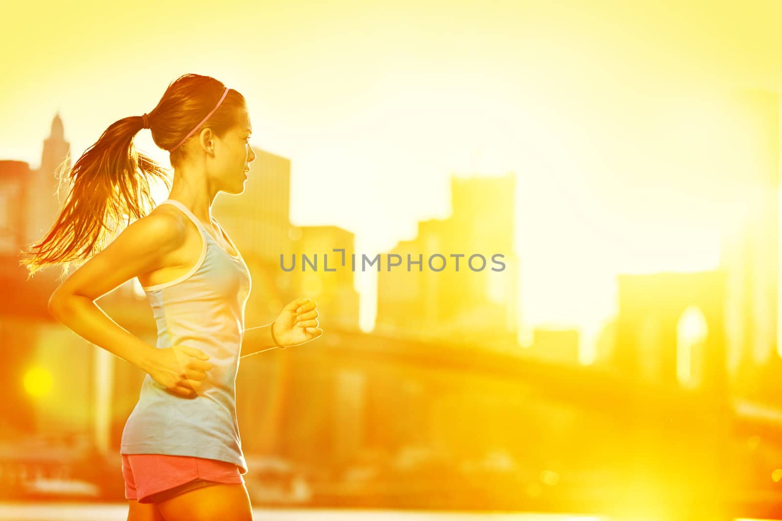 Running woman. Runner jogging in sunny bright light. Female fitness model training outside in New York City with skyline and Brooklyn Bridge in background.