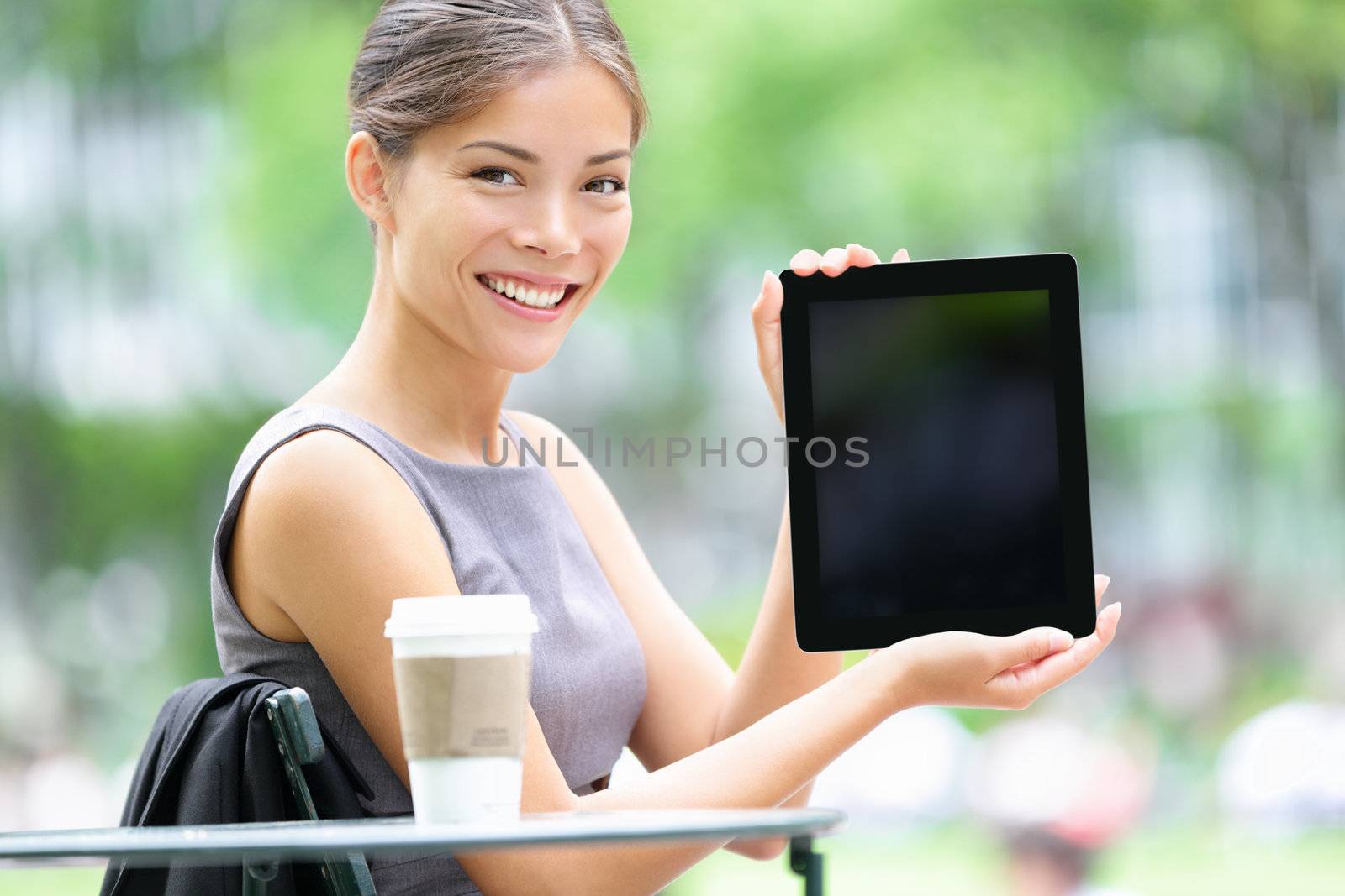 Tablet business woman showing display screen sitting in park. Beautiful young professional businesswoman smiling happy. Mixed race female model. Photo from Bryant Park, Manhattan, New York City.