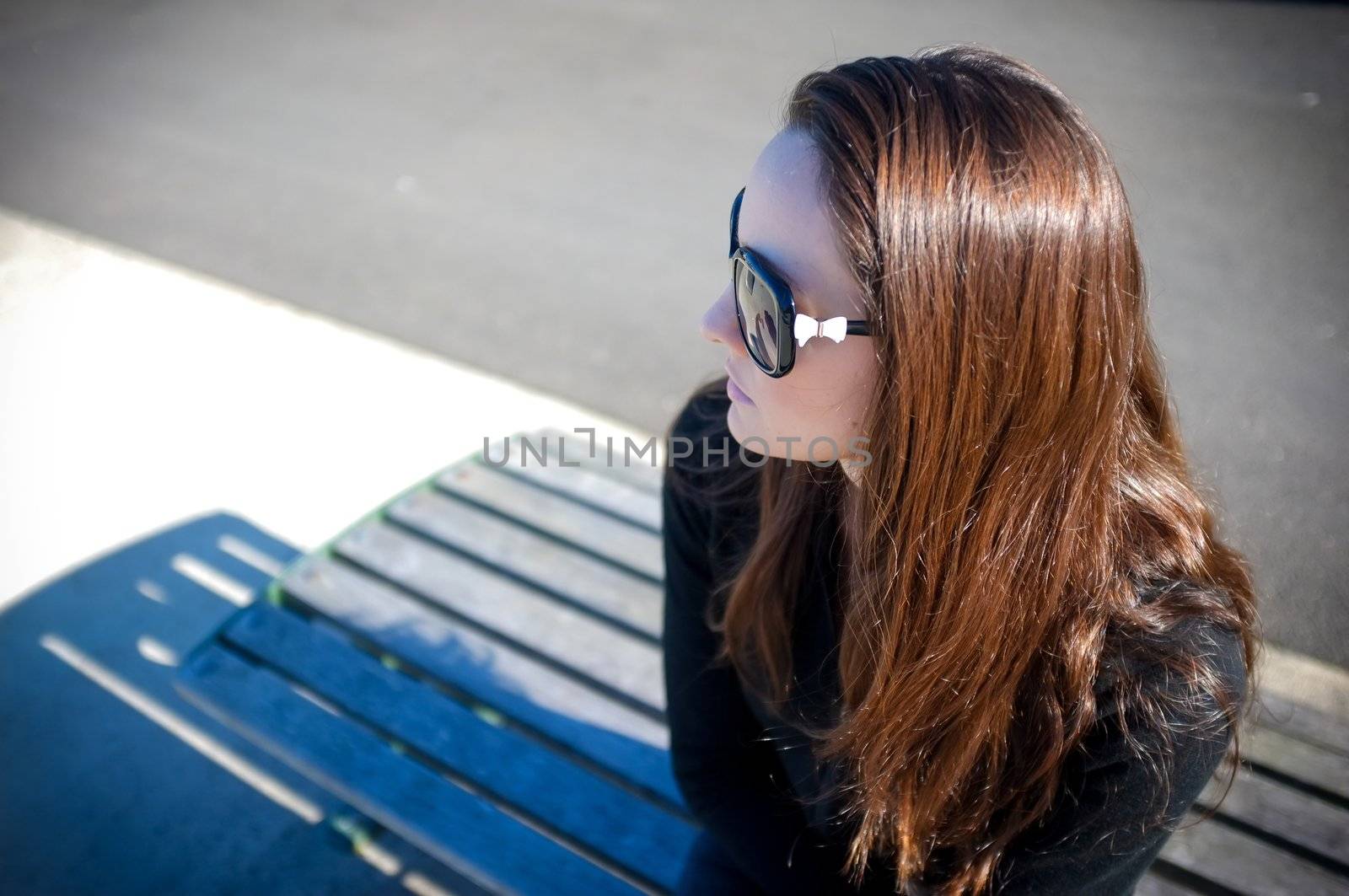 Young beautiful woman in sunglasses sitting on bench at a wharf