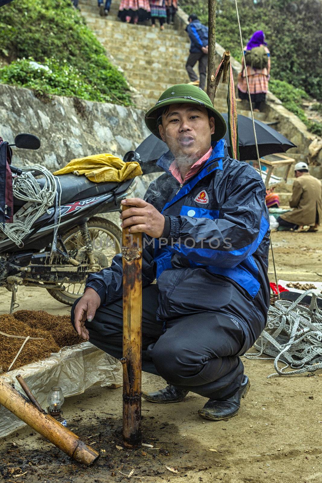 Vietnam Bac Ha - March 2012: Man smoking tobacco in large pipe o by Claudine