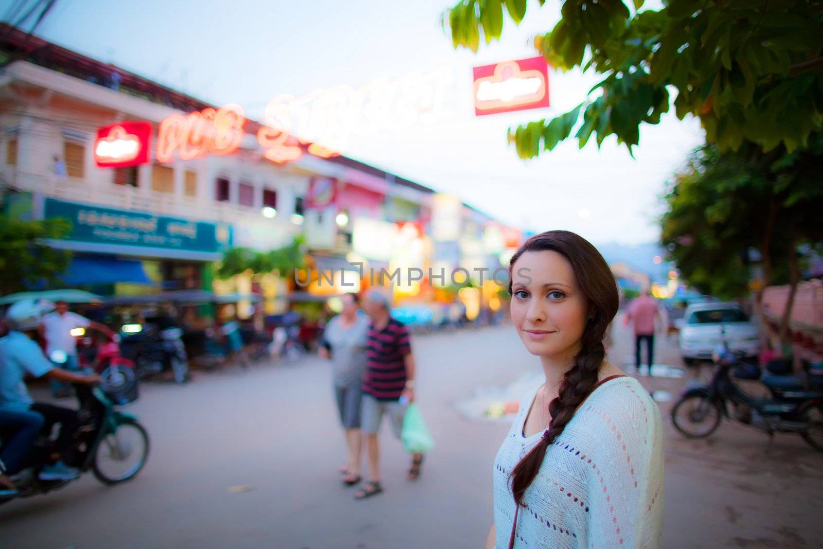 Young caucasian woman close up with plaited hair waiting to cross a busy walk street at dusk in Asia