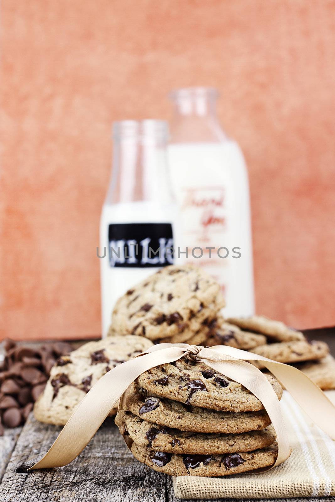 Fresh homemade chocolate chip cookies with chocoate chips and milk in antique milk bottles in the background. Shallow depth of field. 
