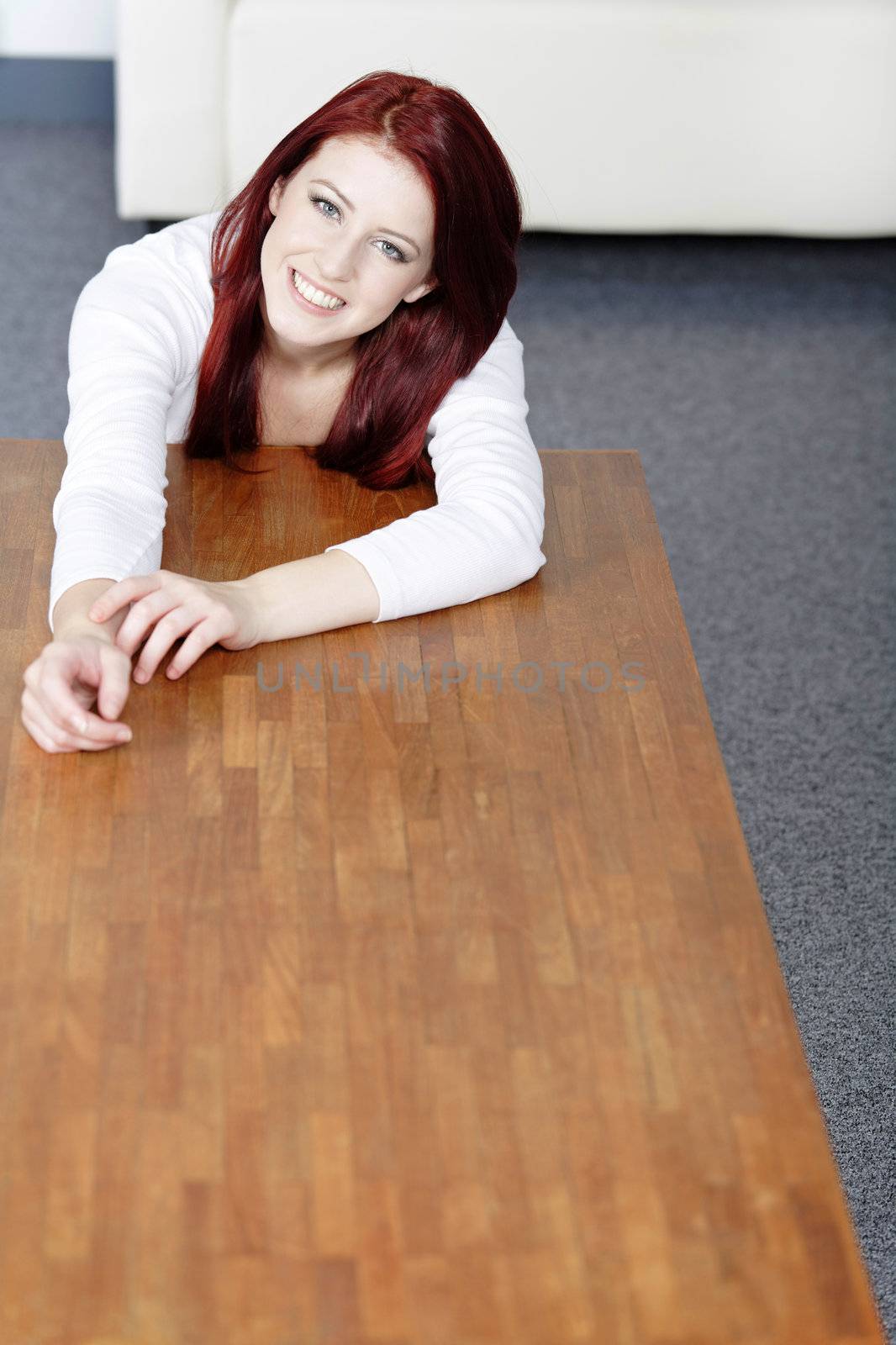 Beautiful young woman resting on a coffee table in front of sofa at home.