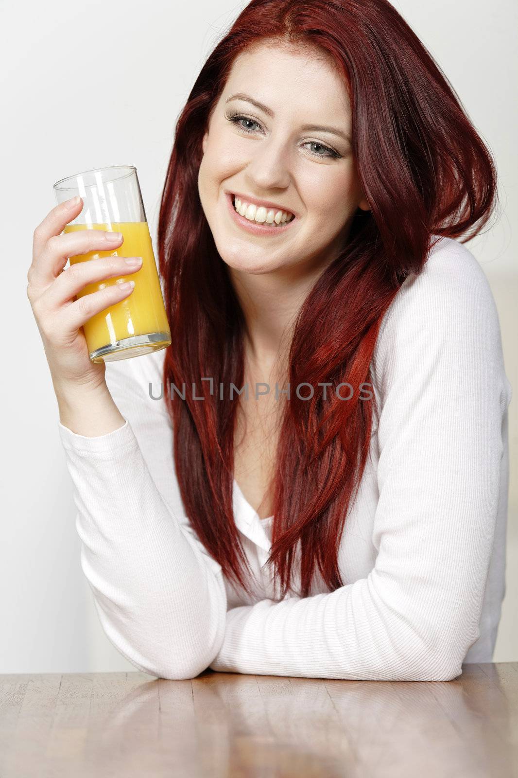 Smiling happy young woman leaning on a wooden table with a fresh glass of Orange juice during breakfast.