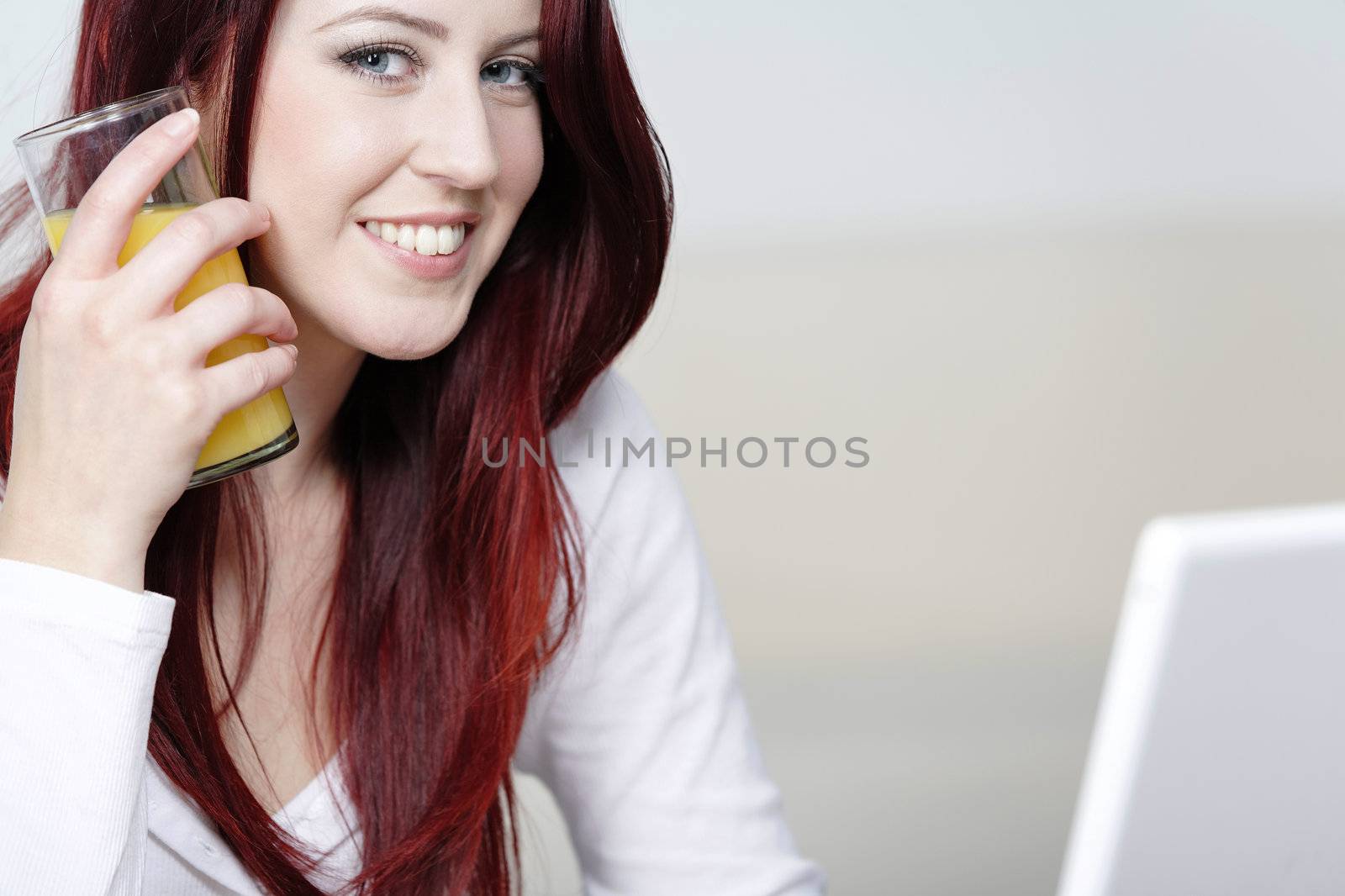 Beautiful young woman using a laptop at home with a fresh glass of Orange juice.