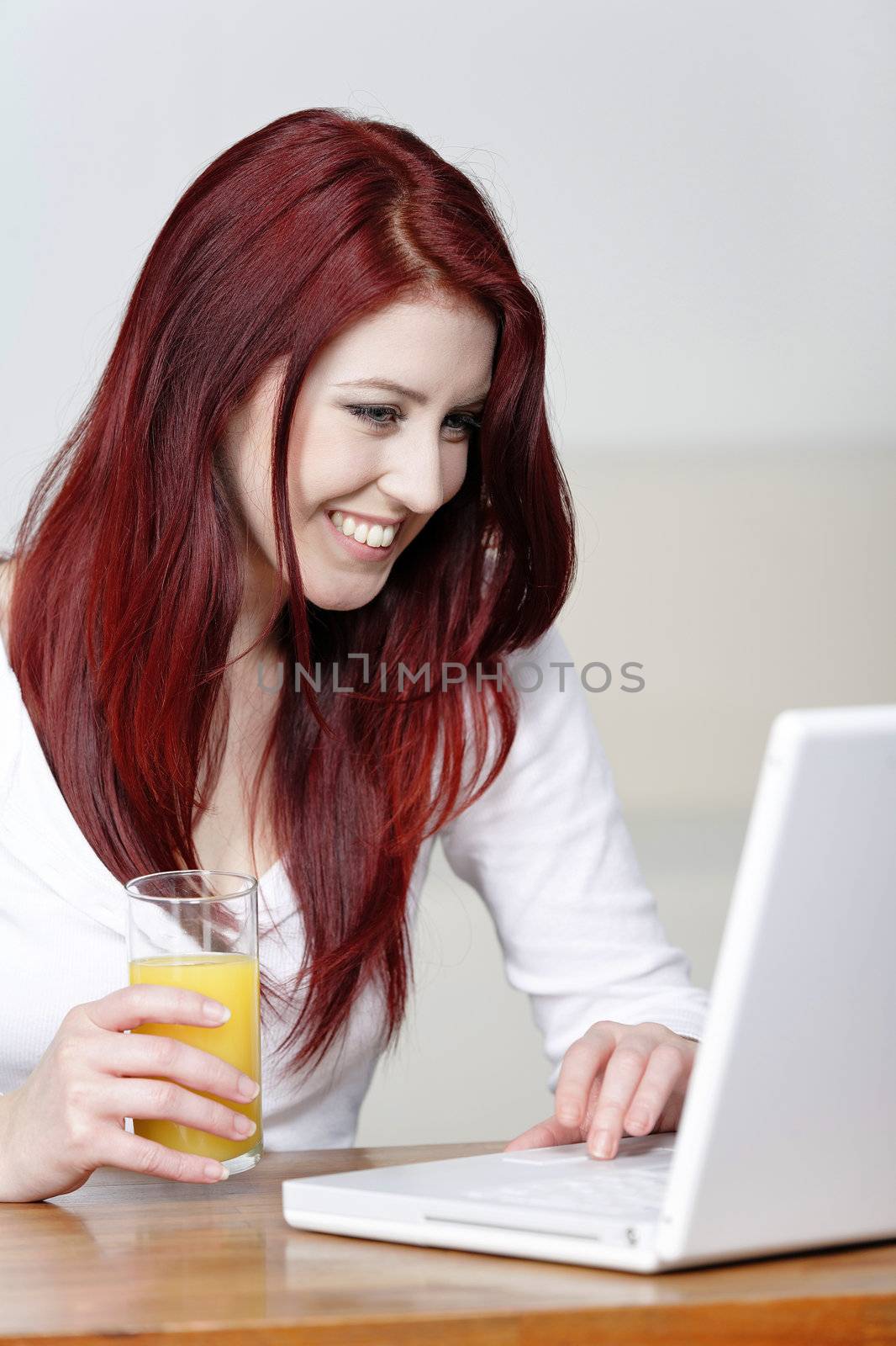 Beautiful young woman using a laptop at home with a fresh glass of Orange juice.