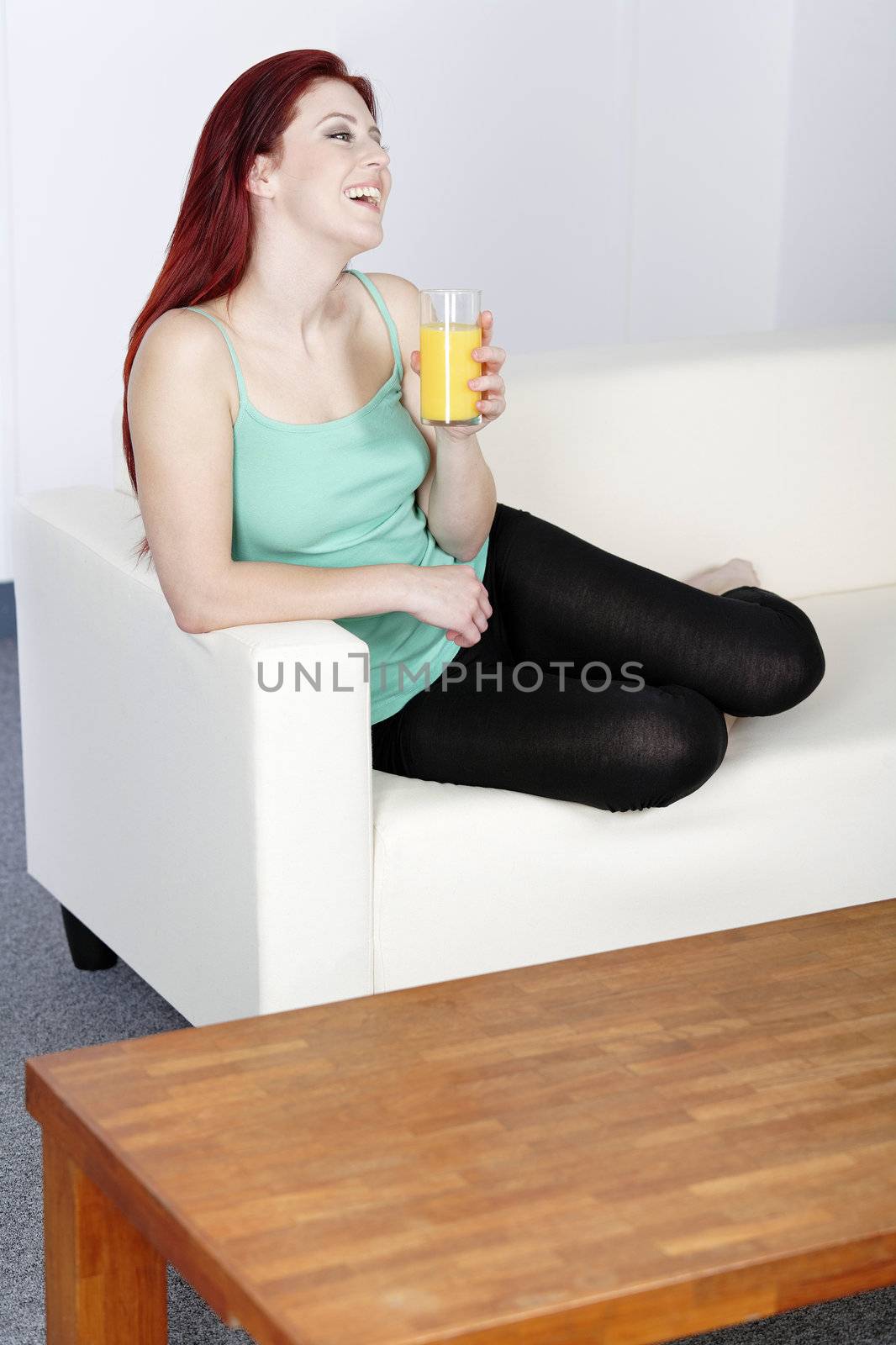 Happy smiling young woman drinking fresh Orange juice at home on the sofa