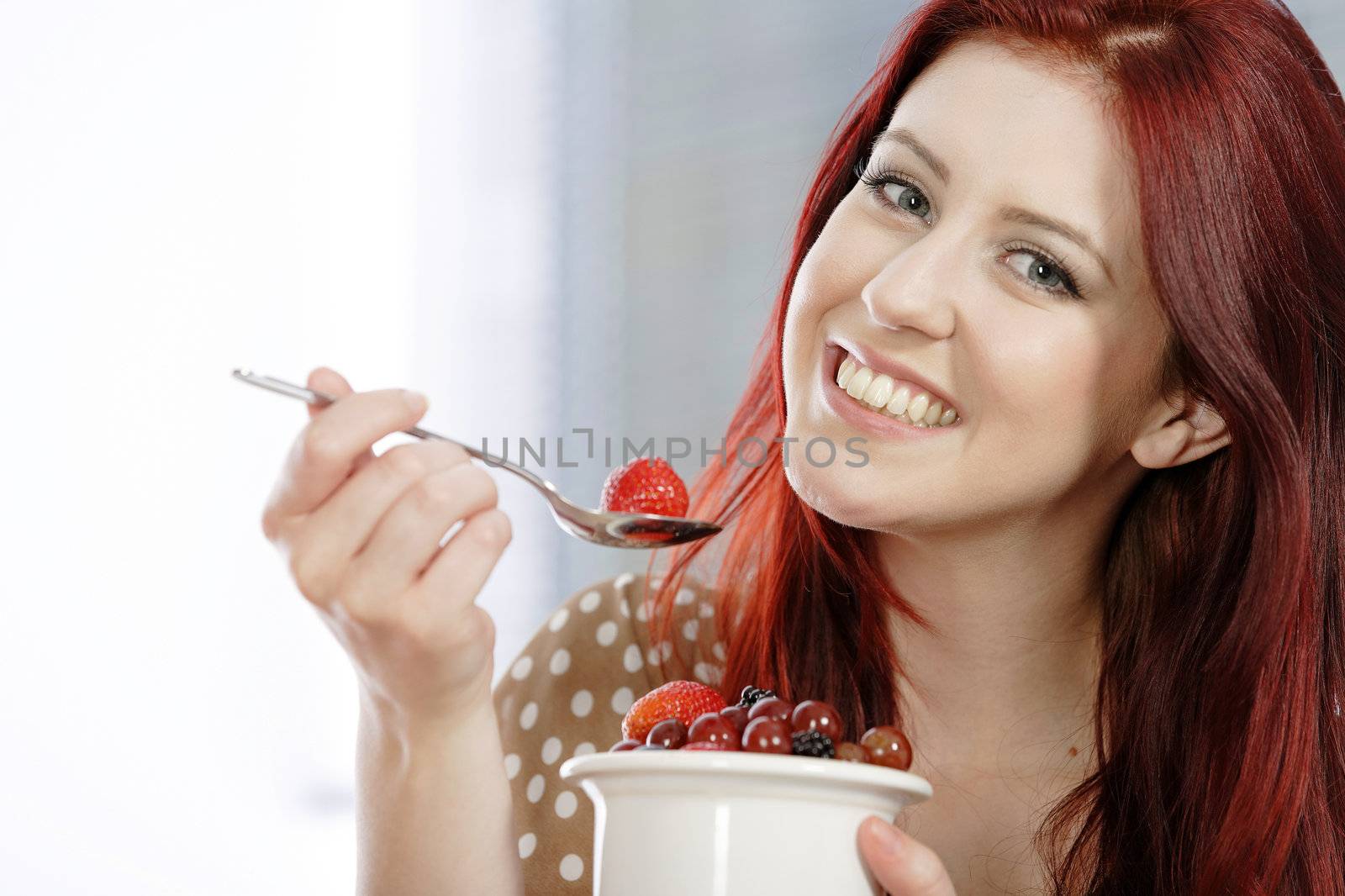 Happy smiling young woman enjoying a fresh bowl of fruit for breakfast.