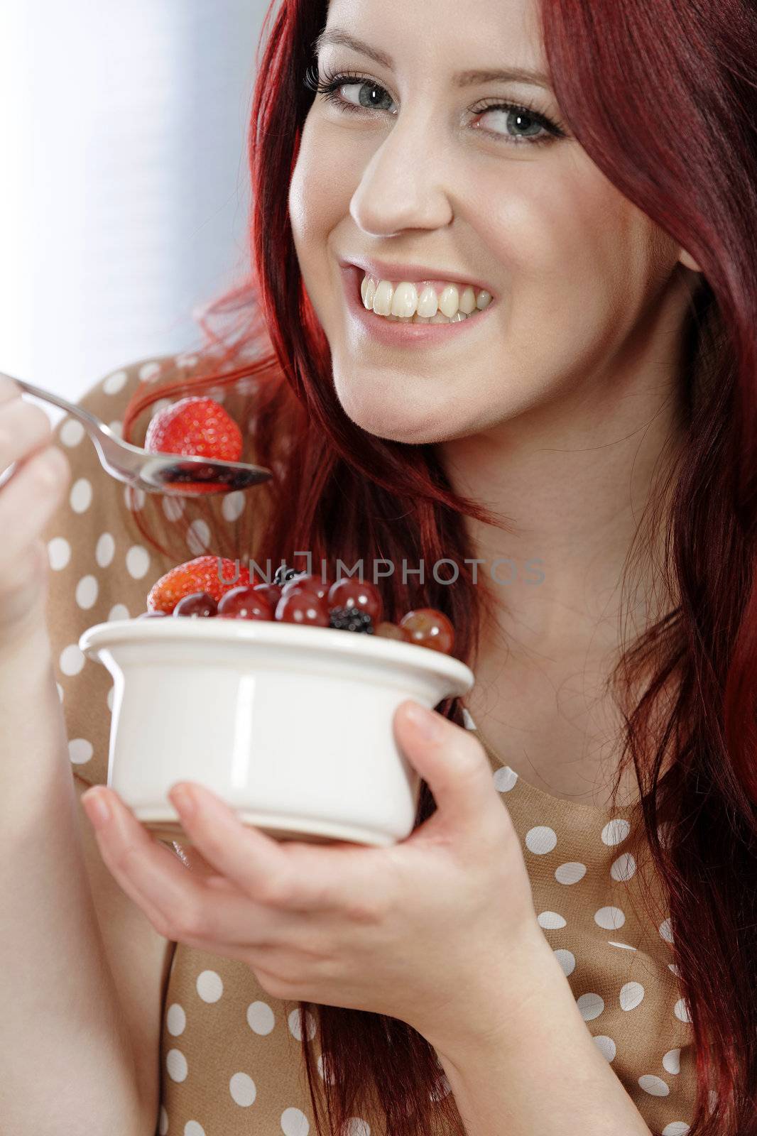 Happy smiling young woman enjoying a fresh bowl of fruit for breakfast.