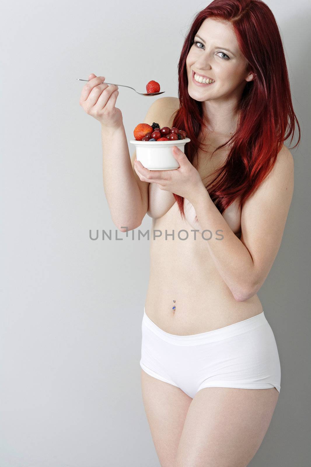 Happy young woman eating a bowl of fresh fruit in her underwear at home