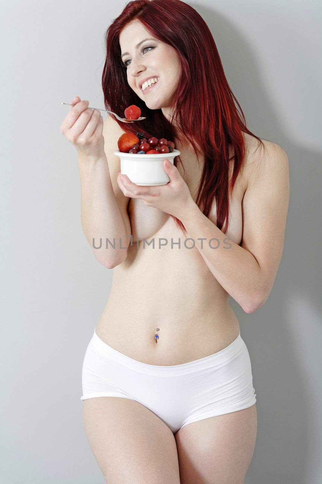 Happy young woman eating a bowl of fresh fruit in her underwear at home