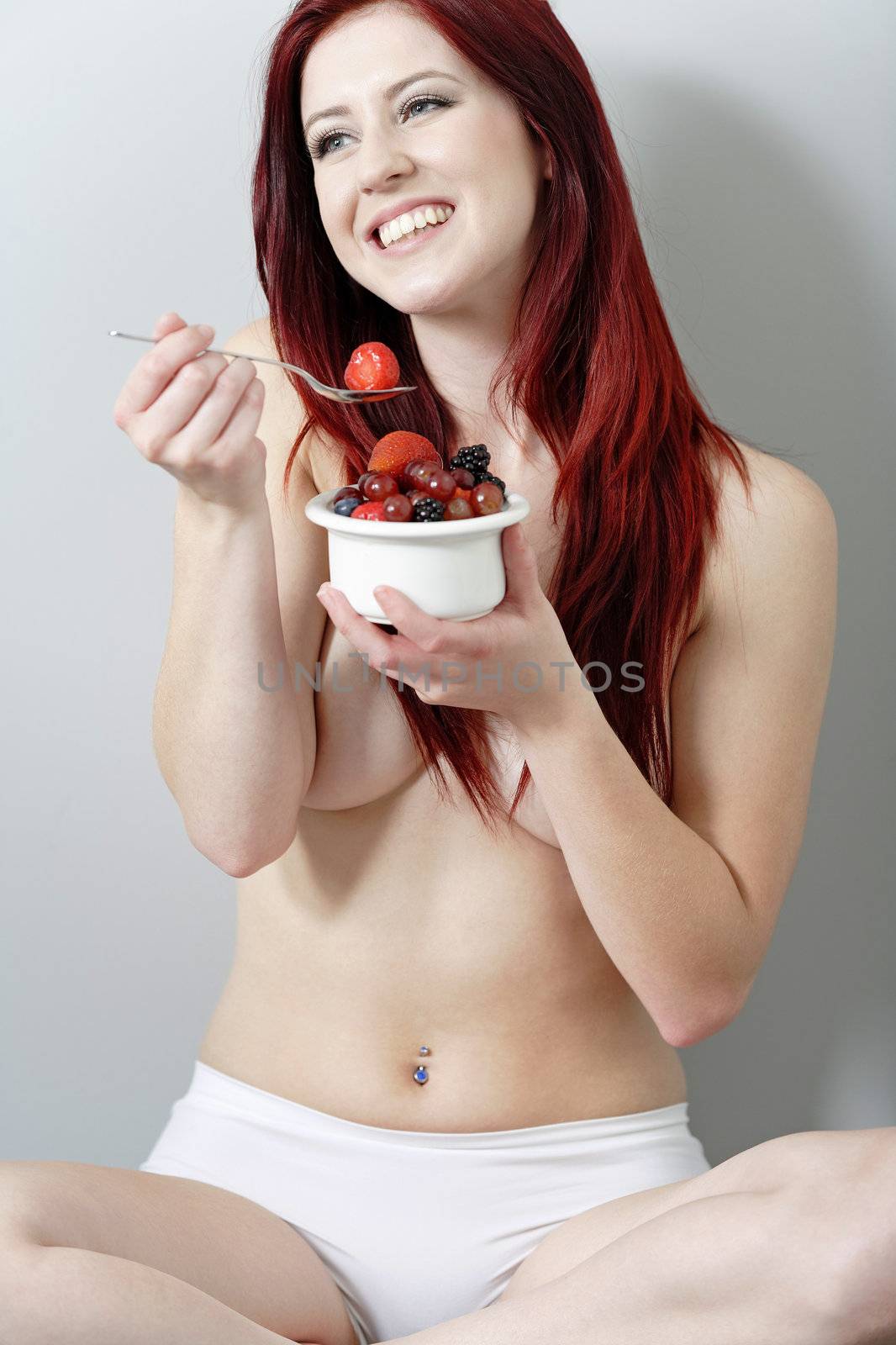 Beautiful young woman sat against a wall enjoying a bowl of fresh fruit