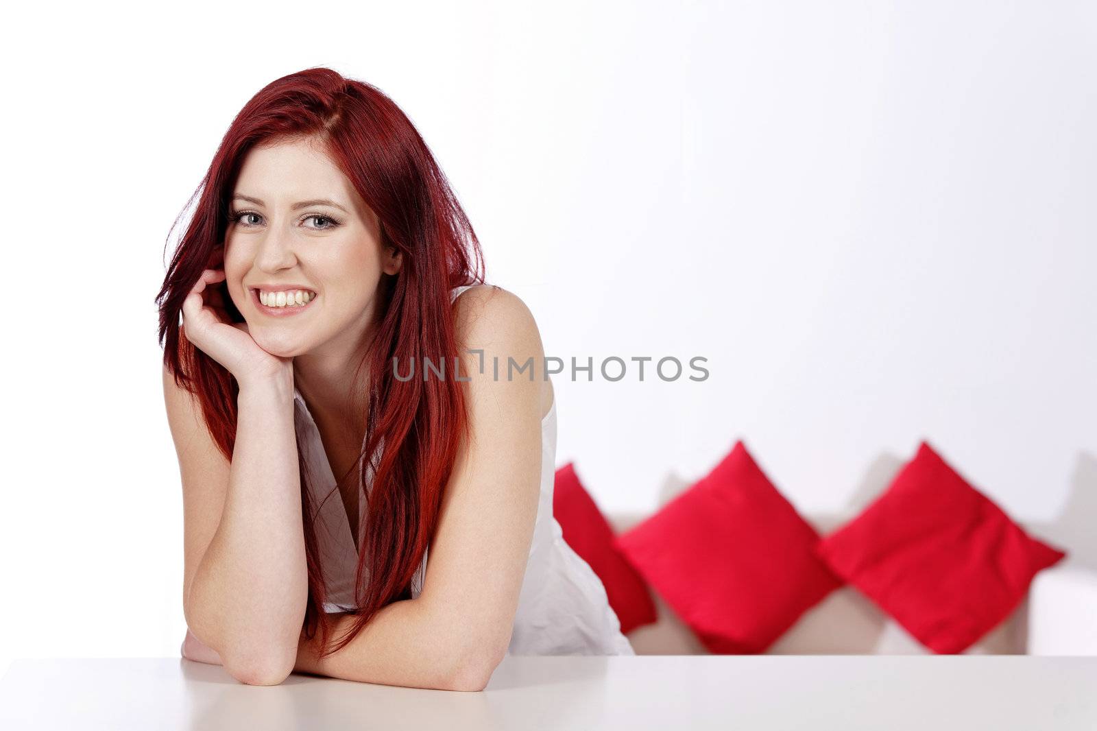 Beautiful young woman leaning on a table at home with a sofa in the background.