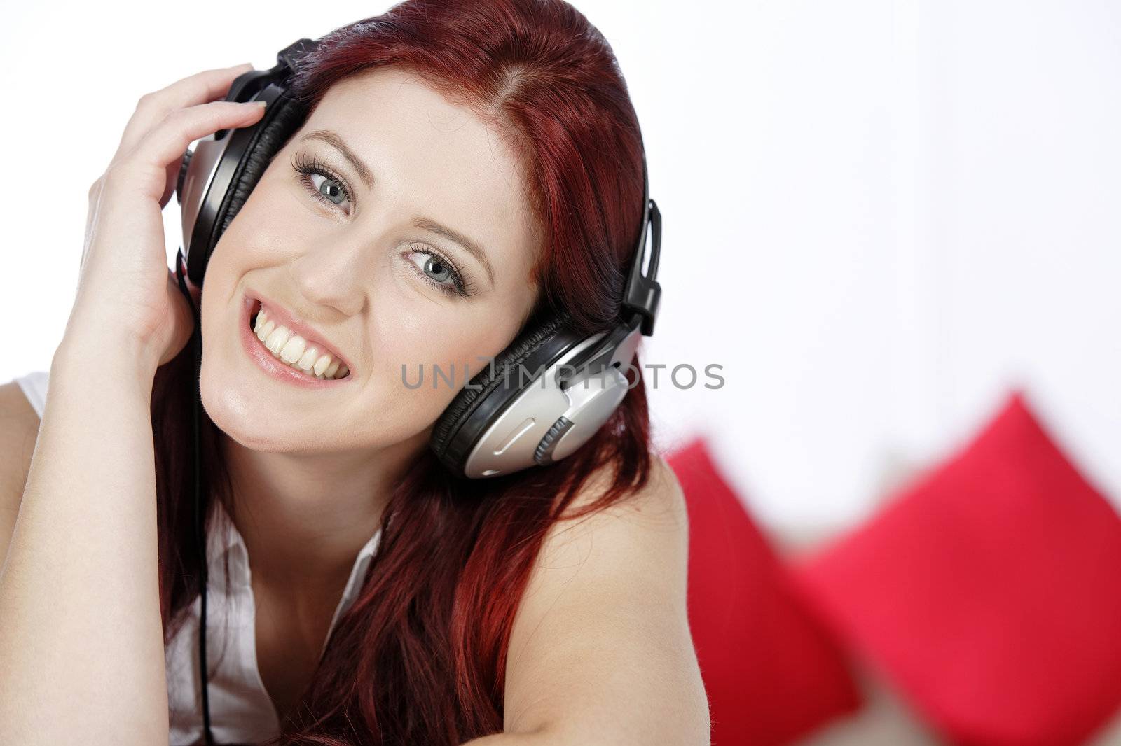 Beautiful young woman lying on her sofa at home listening to music on her headphones