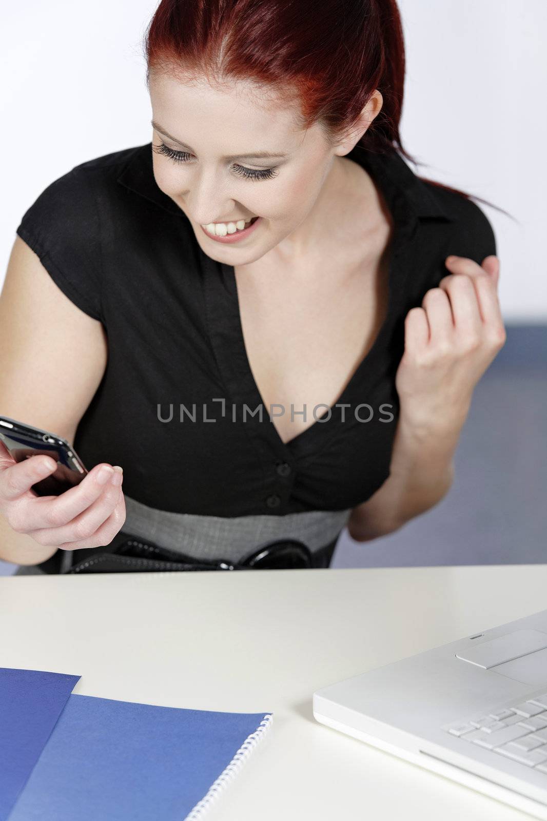Professional young woman receiving good news on her mobile at work