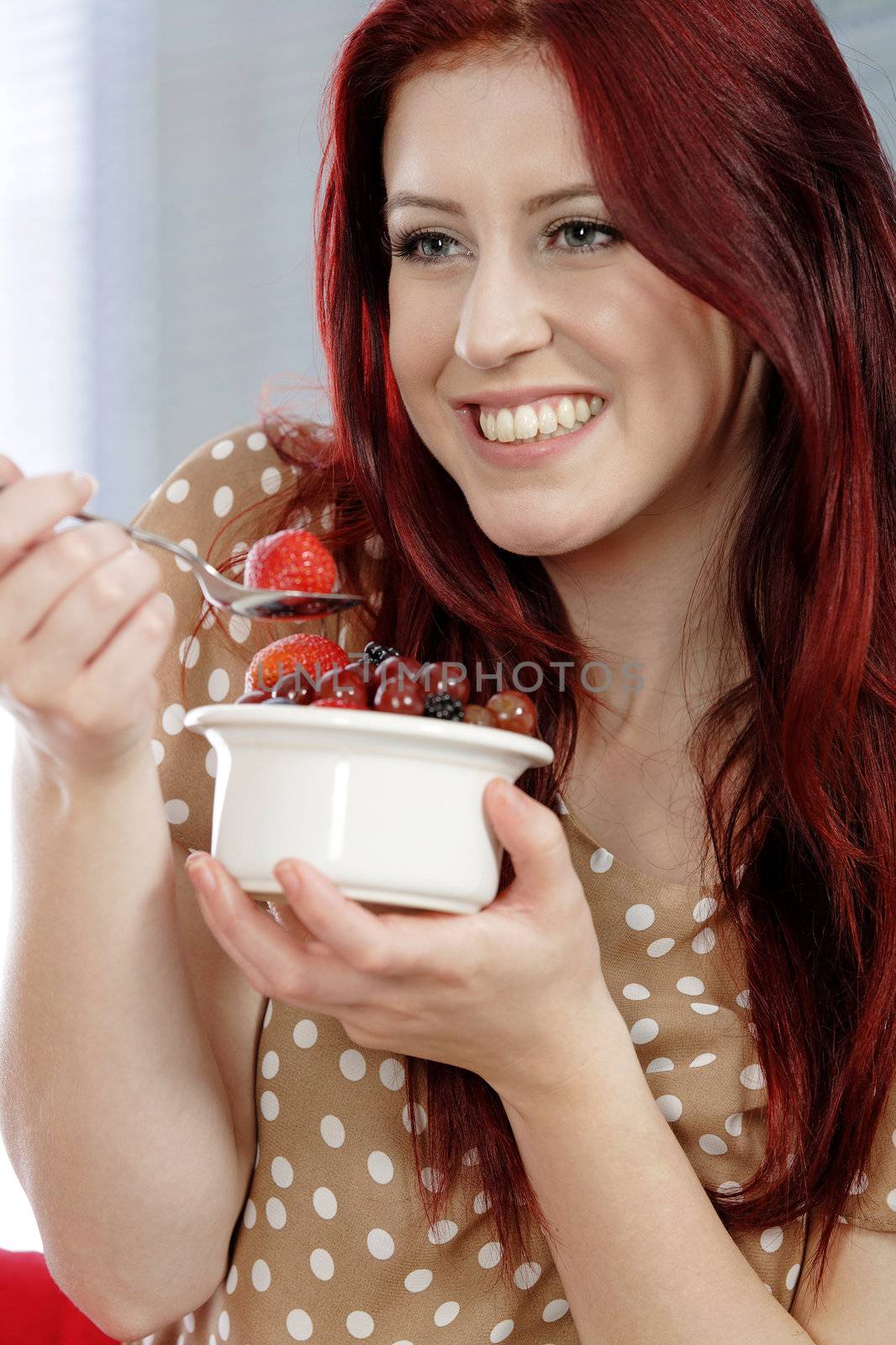 Happy smiling young woman enjoying a fresh bowl of fruit for breakfast.