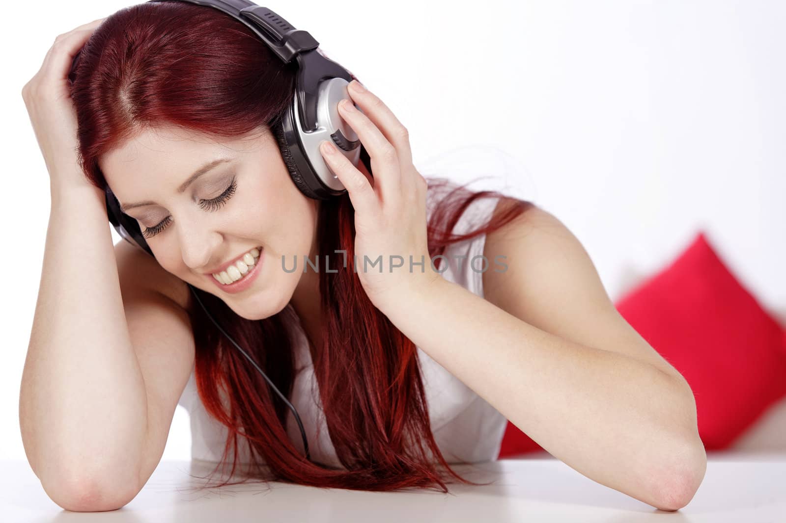 Beautiful young woman lying on her sofa at home listening to music on her headphones