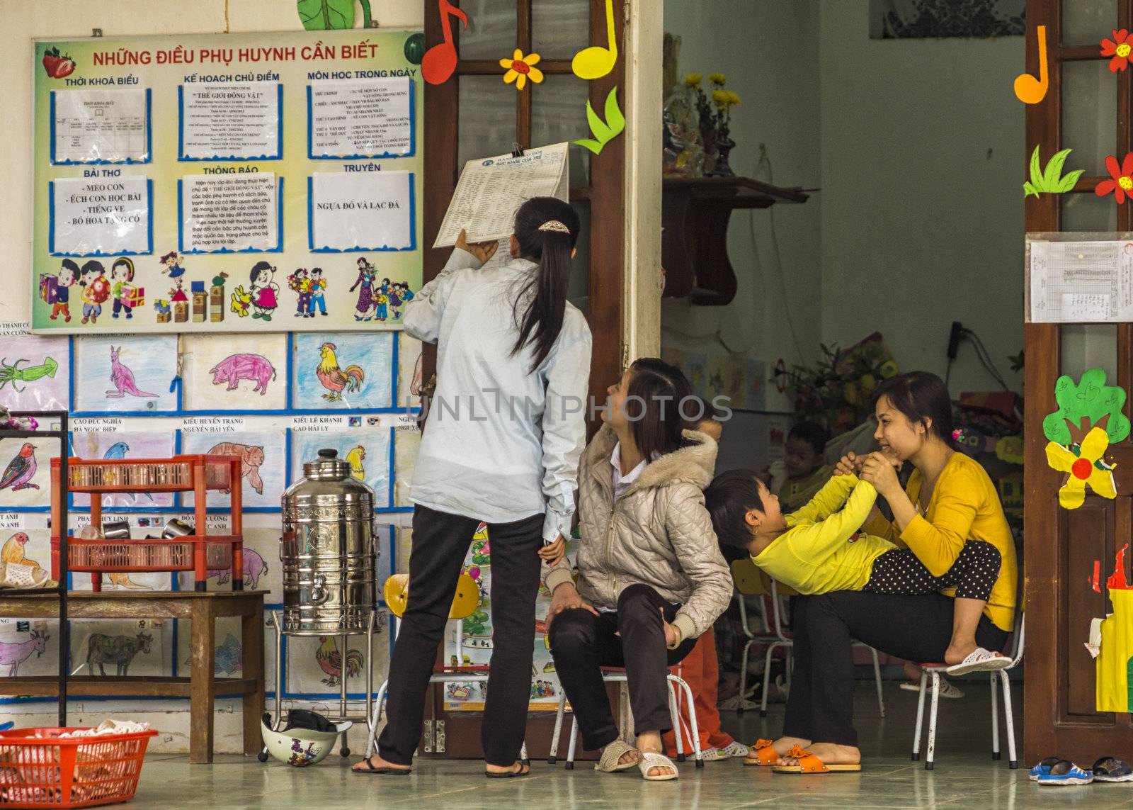 Vietnam Duong Lam. Three teachers check schedule against decor of children's drawings.