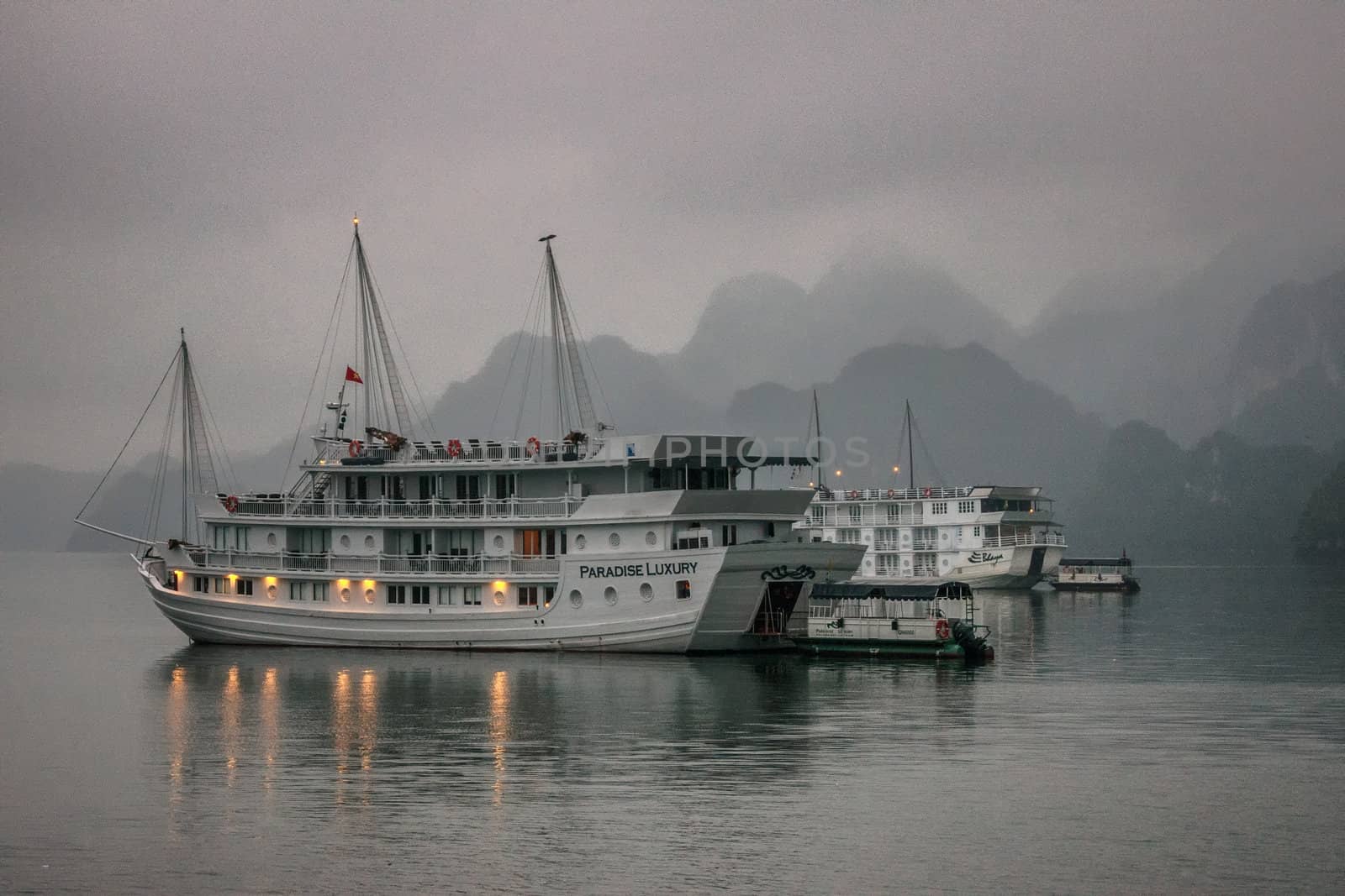 Cruise junk boat sitting under early morning fog in front of limestone mountains. by Claudine