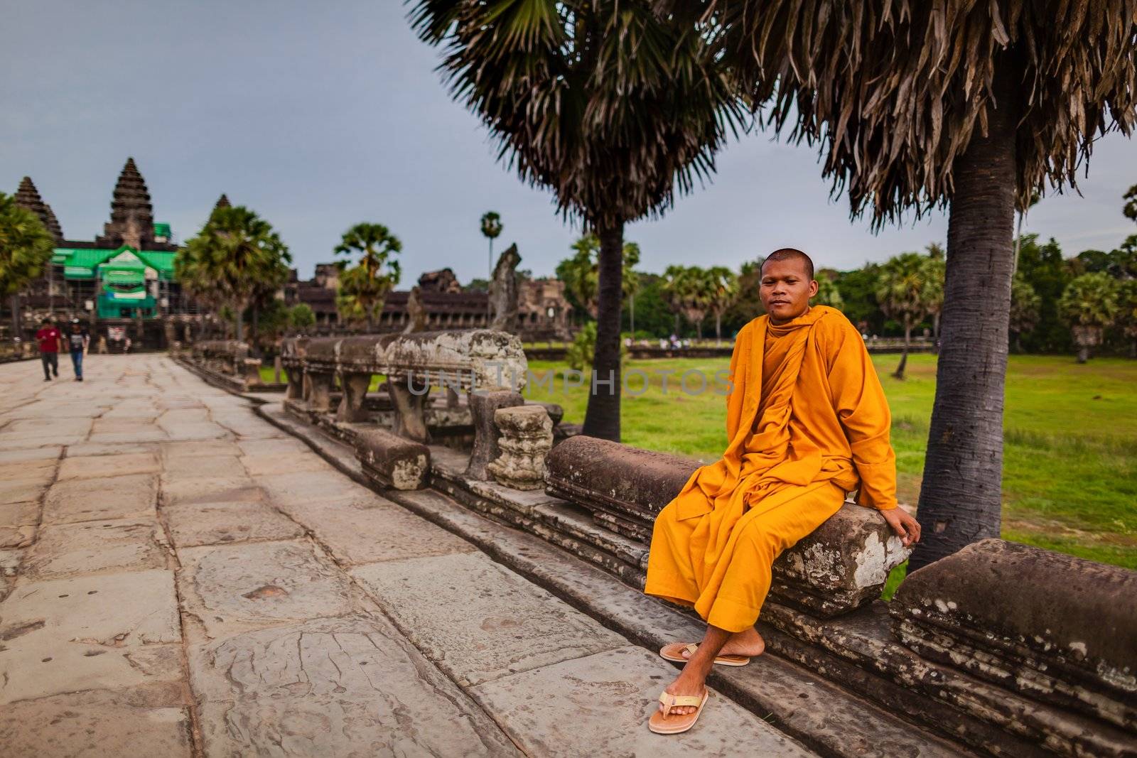 SIEM REAP, CAMBODIA - CIRCA JUNE 2012: Unidentified buddhist monk sits on the edge of the causeway/walkway circa June 2012 in Angkor Wat, Cambodia The monastery is still use as part of worship sacred place.