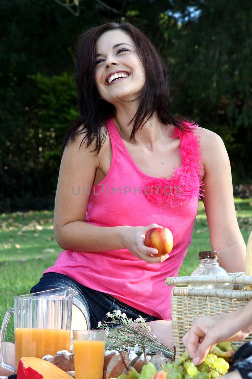 Gorgeous smiling brunette woman eating an apple at an outdoor picnic
