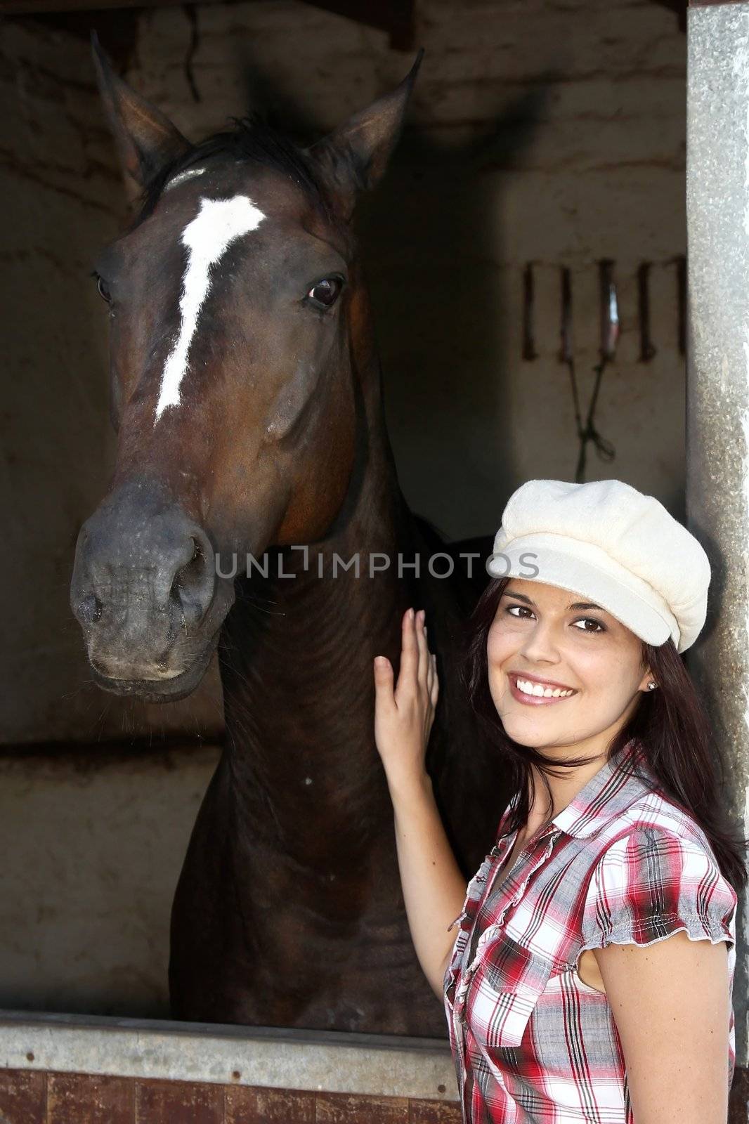 Beautiful smiling brunette woman with her horse in a stable